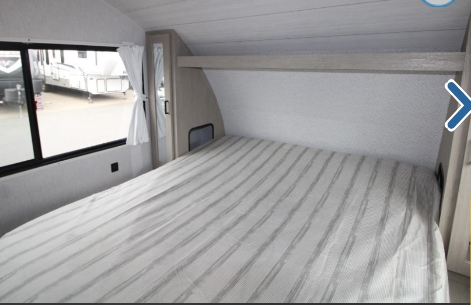 View of an RV rental's bedroom: striped bed, window, and built-in storage.. Forest River Wildwood XLite View 2024