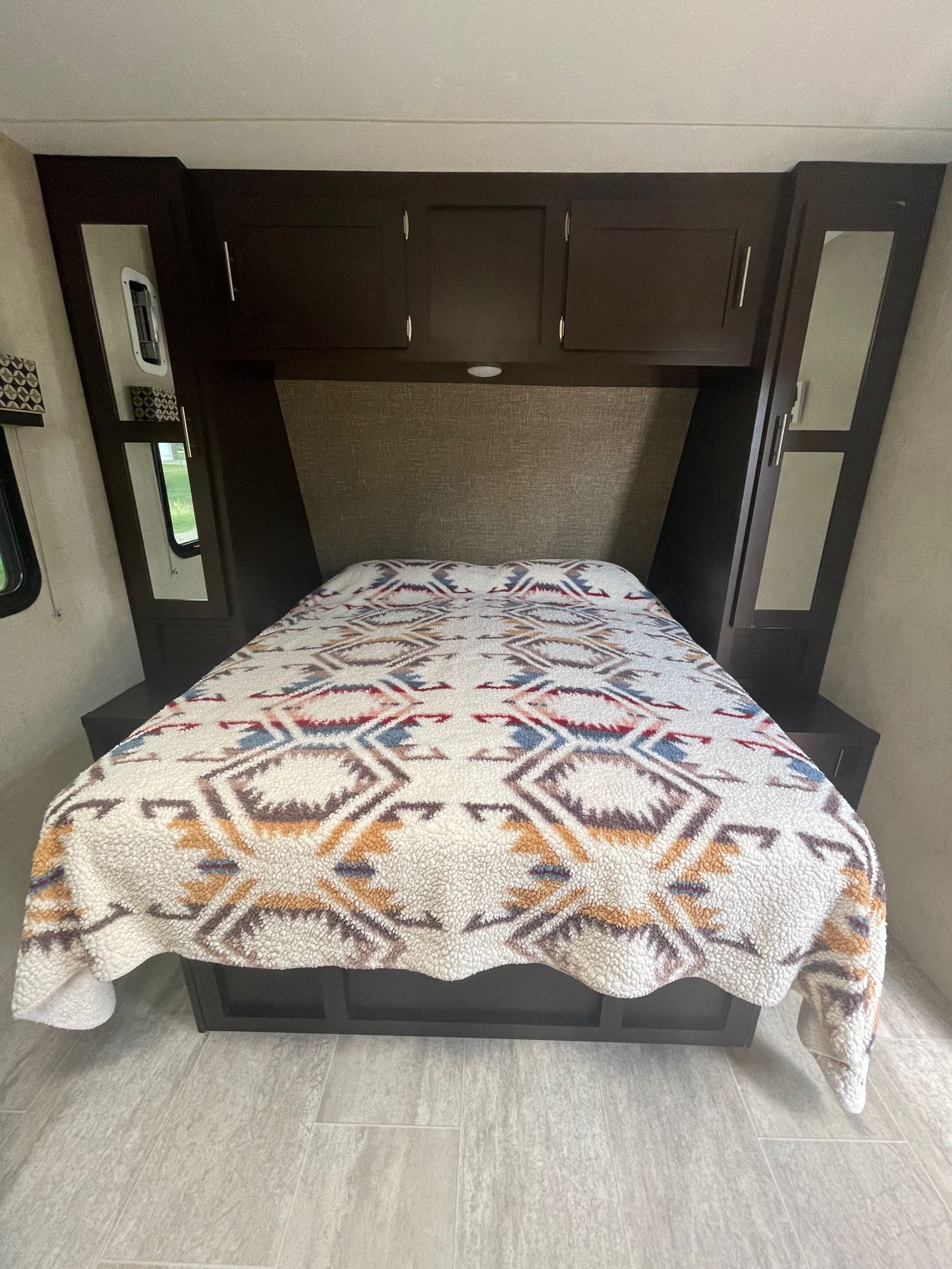 Relaxing RV rental bedroom featuring a bed with a vibrant tribal-patterned blanket, built-in dark wood cabinetry, and mirrored closets.. K-Z Manufacturing Sportster 2018