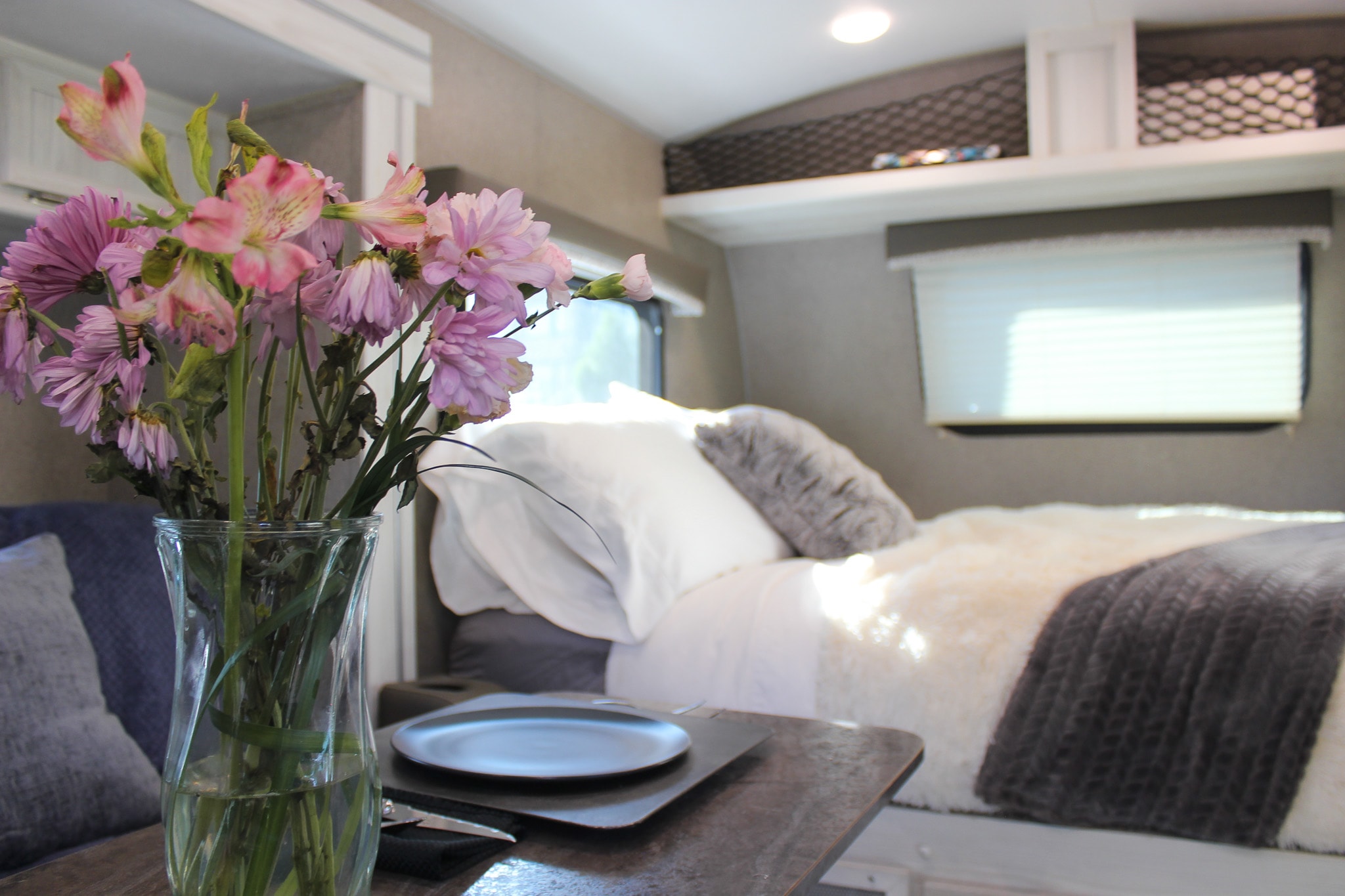 Inside a comfy RV rental: bright bed area with soft throws, overhead storage, and a vase of flowers.. Forest River Rockwood GeoPro 2019
