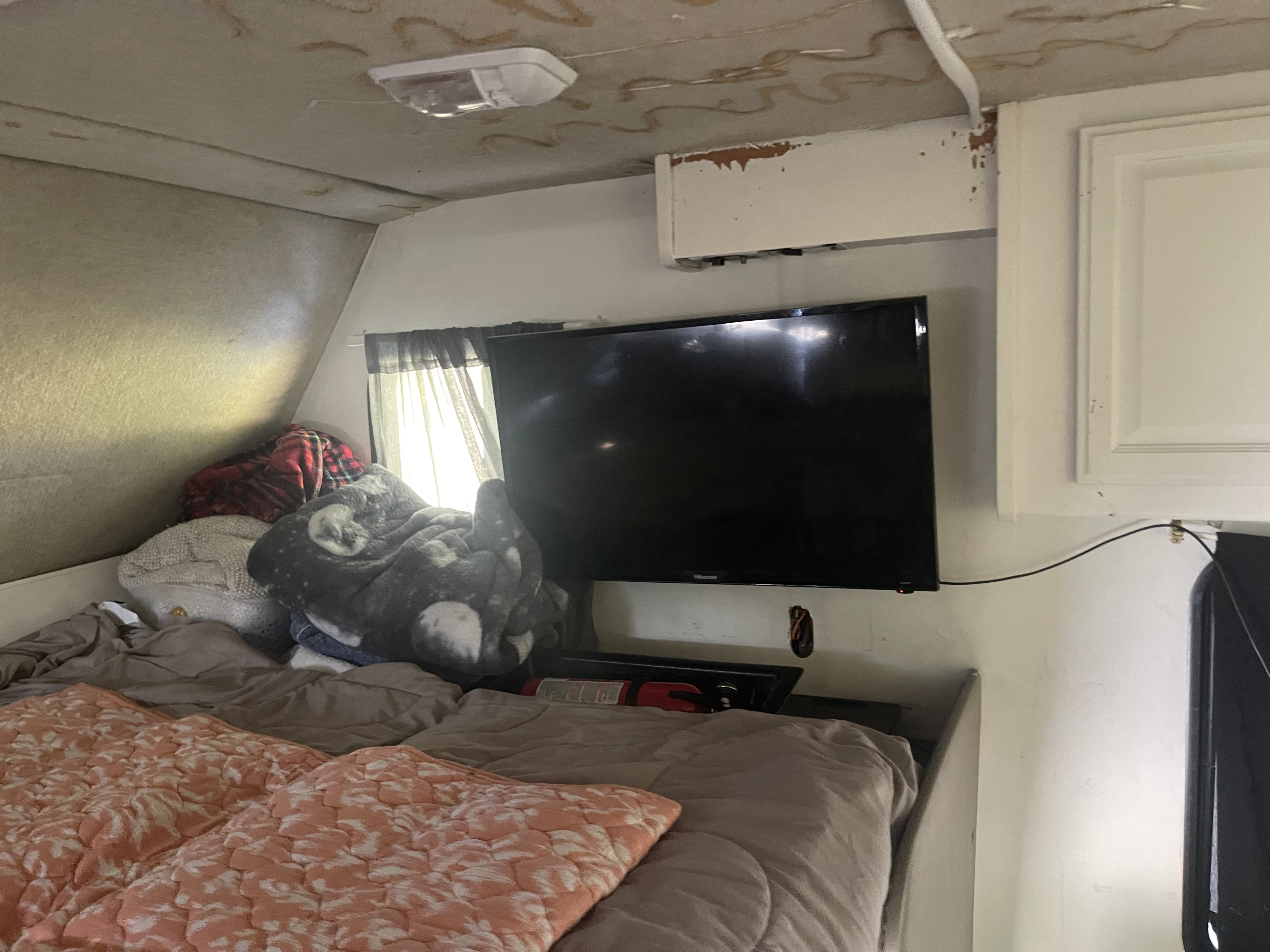 RV rental interior: cozy bedroom with a bed, blankets, wall-mounted TV, and fire extinguisher visible.. Jamboree Sport 2012