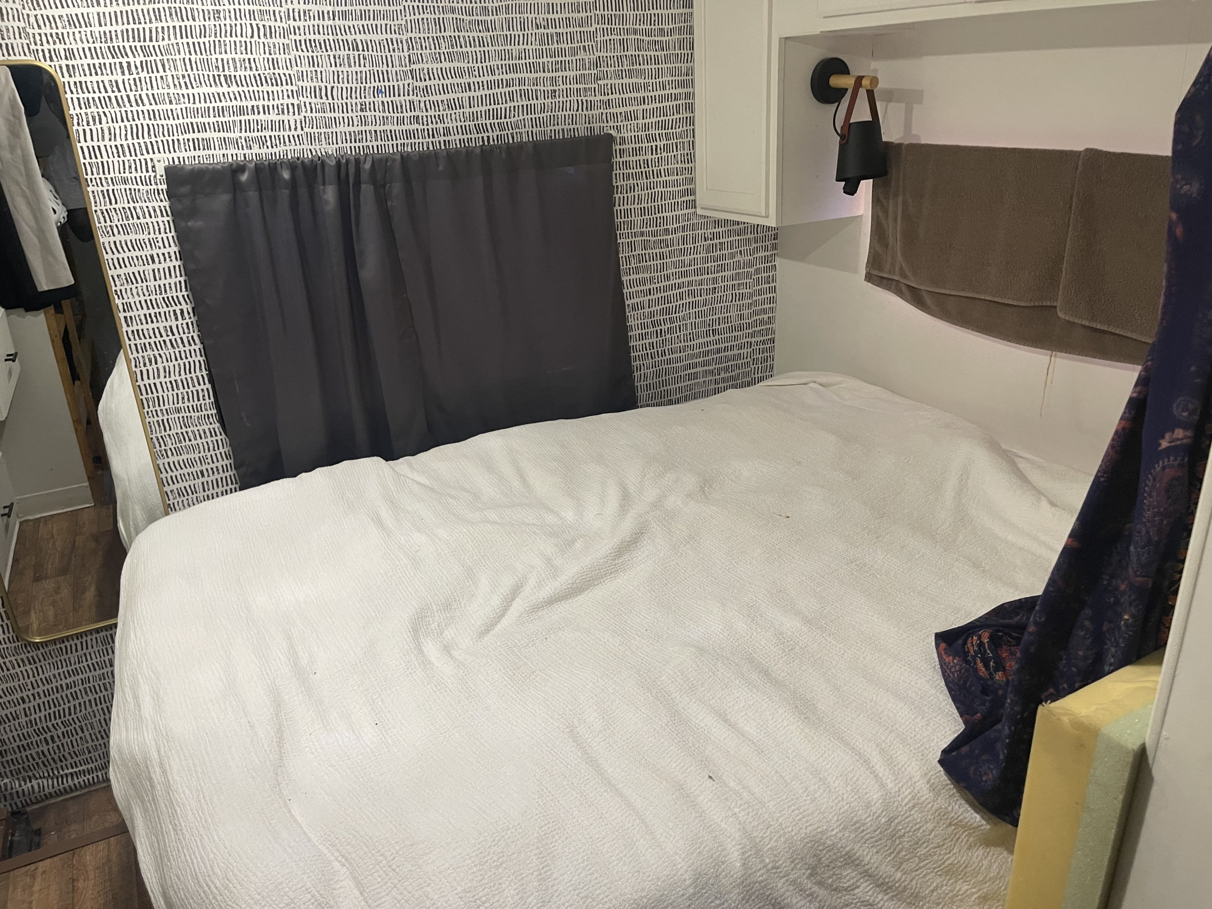 Cozy RV rental bedroom featuring a white bed with textured bedding, abstract black and white wallpaper, and practical overhead storage.. Jamboree Sport 2012