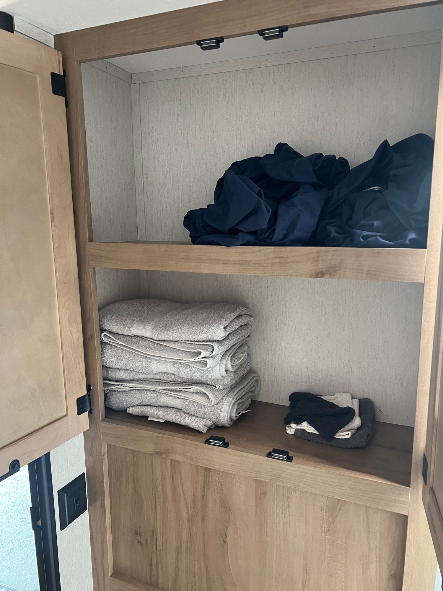 RV rental storage: Wooden cabinet shows folded towels, dark bedding/clothes, and small washcloths, providing practical space.. Forest River Cherokee Grey Wolf 2024