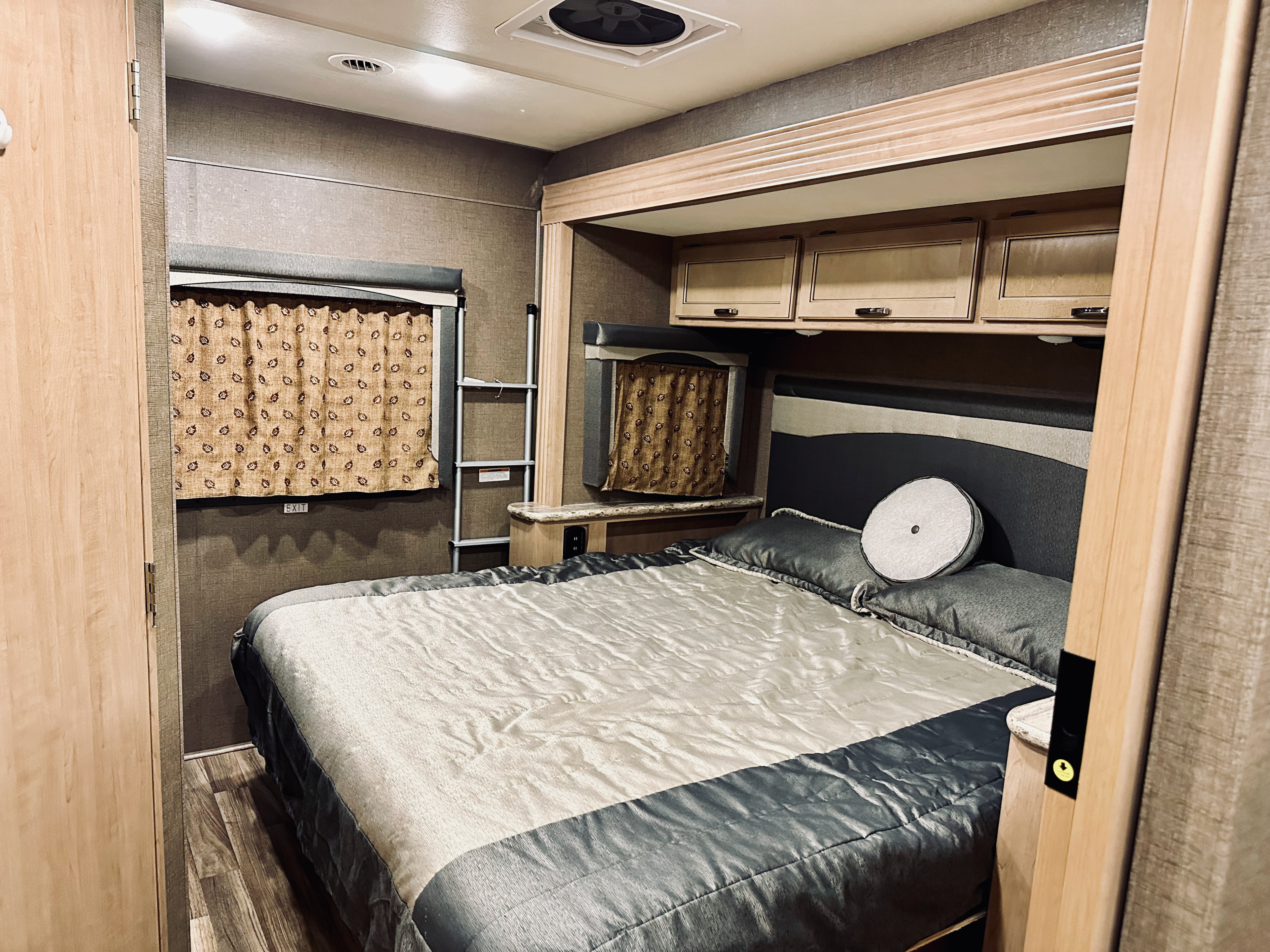 Inside an RV rental: a spacious bedroom featuring a queen bed, overhead cabinets, and a ladder leading to a top bunk.. Thor A.C.E. 2018