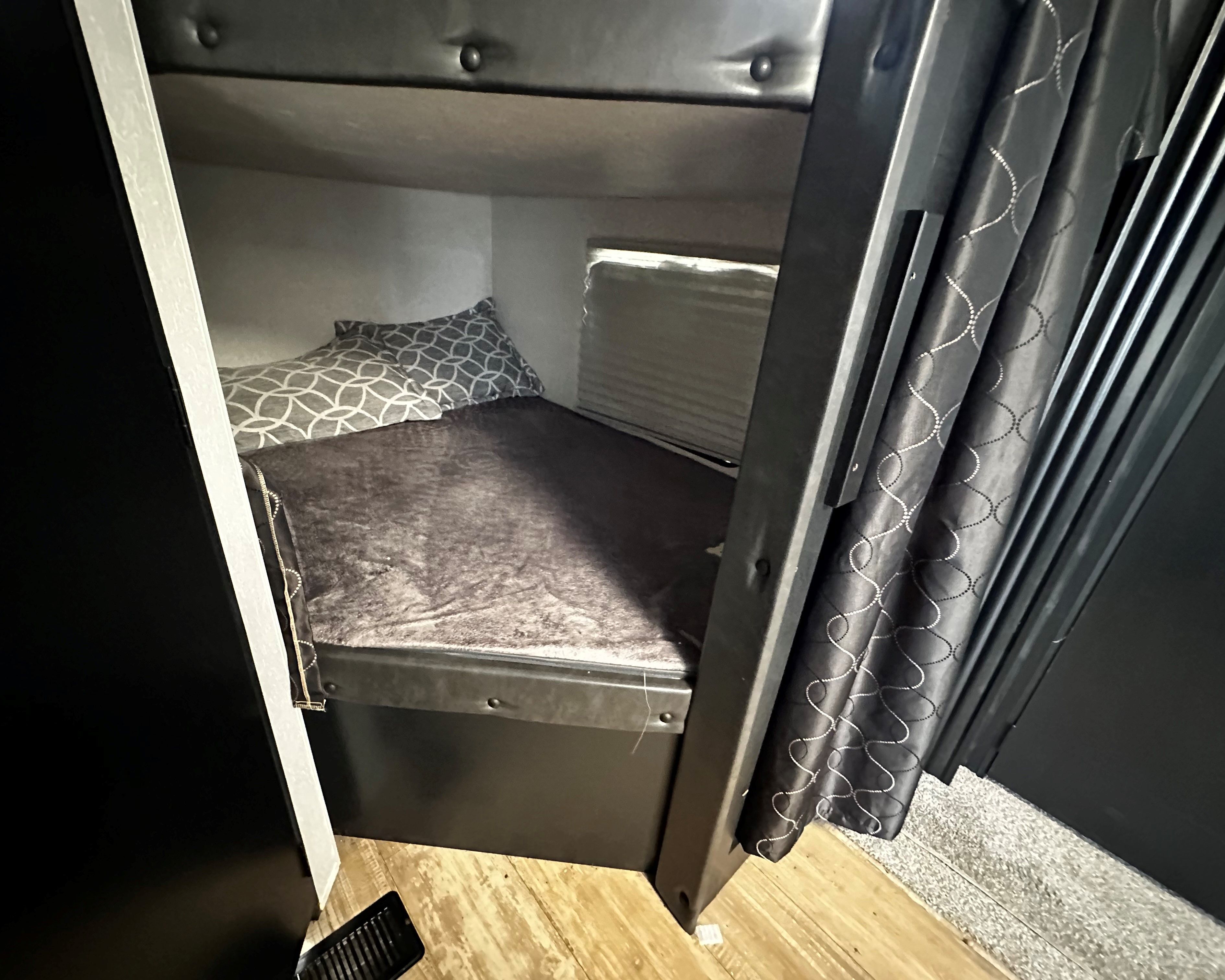 Cozy dark grey bunk bed inside an RV rental, complete with a patterned pillow and window blinds.. Forest River Cherokee 2021