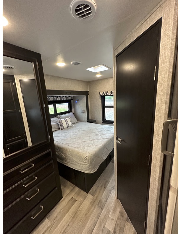 Inside an RV rental, this clean bedroom offers a comfortable bed, light wood-look flooring, dark cabinetry, and windows.. Entegra Coach Odyssey 2022