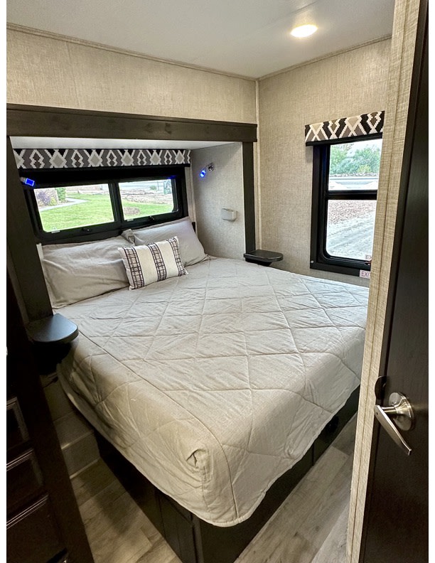 Cozy RV rental bedroom features a spacious bed, large windows with outdoor views, and built-in nightstands for comfort.. Entegra Coach Odyssey 2022
