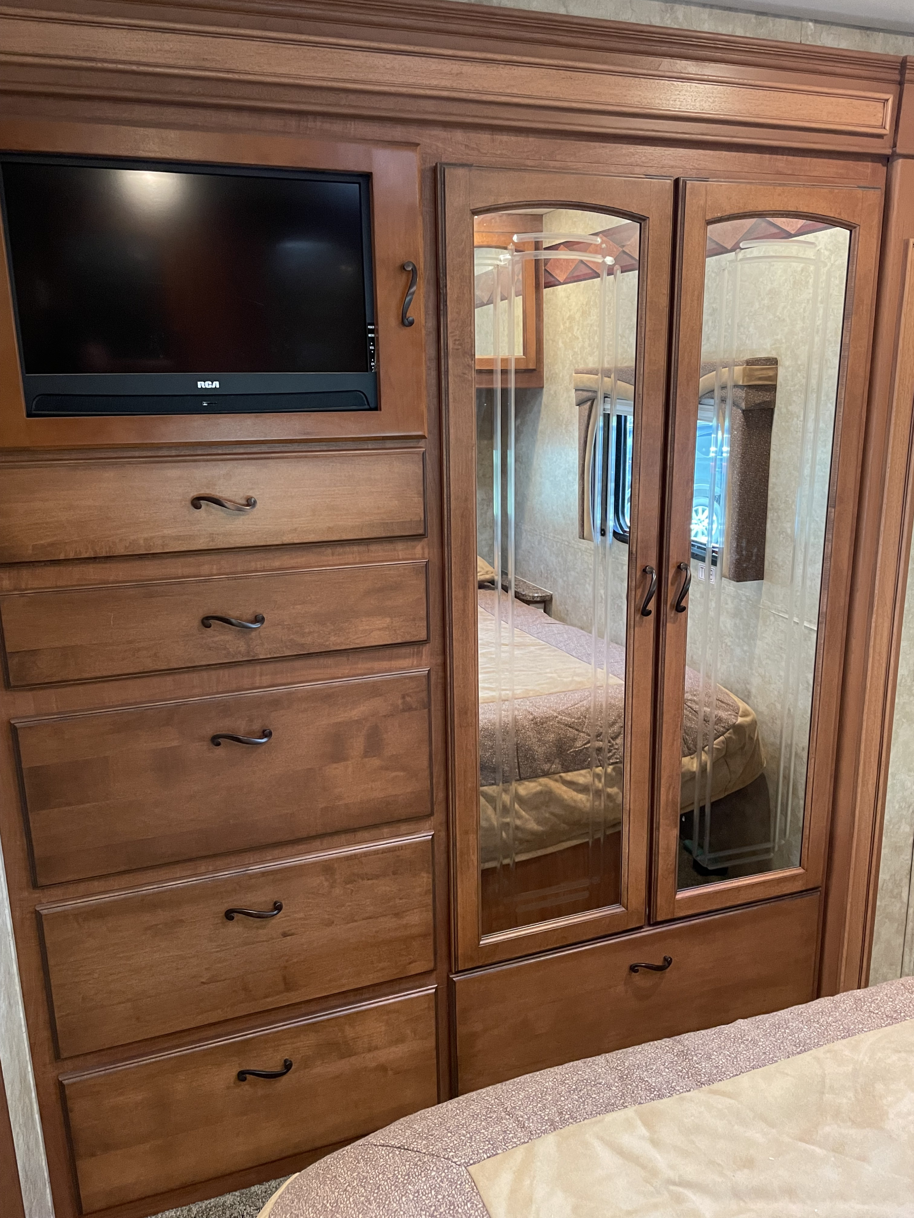 Cozy RV rental bedroom featuring built-in wooden dresser, TV, and mirrored wardrobe, optimizing space and storage.. Jayco Greyhawk 2010