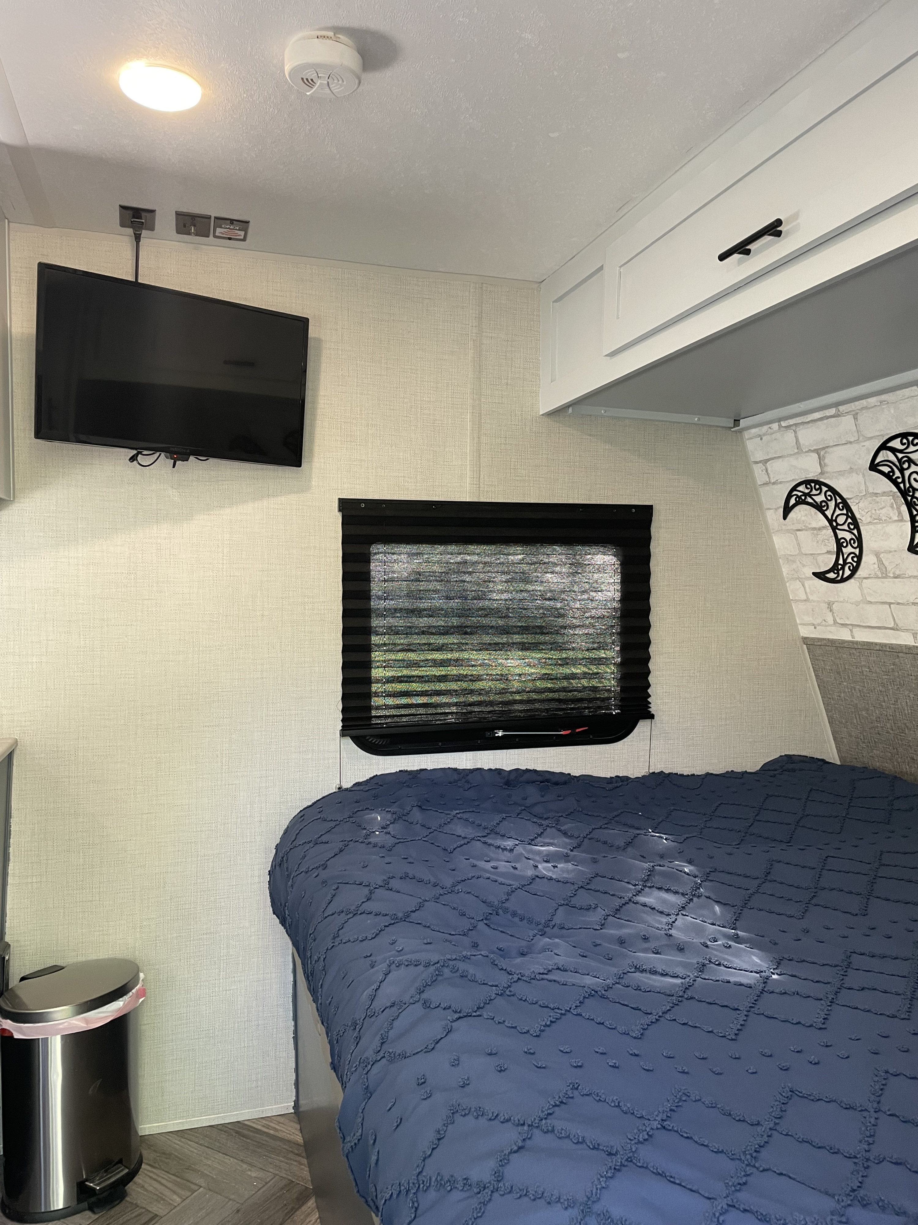 Comfortable RV rental bedroom showcasing a blue bed, wall-mounted TV, window, and bright overhead storage.. Forest River Ozark 1650BHK 2021