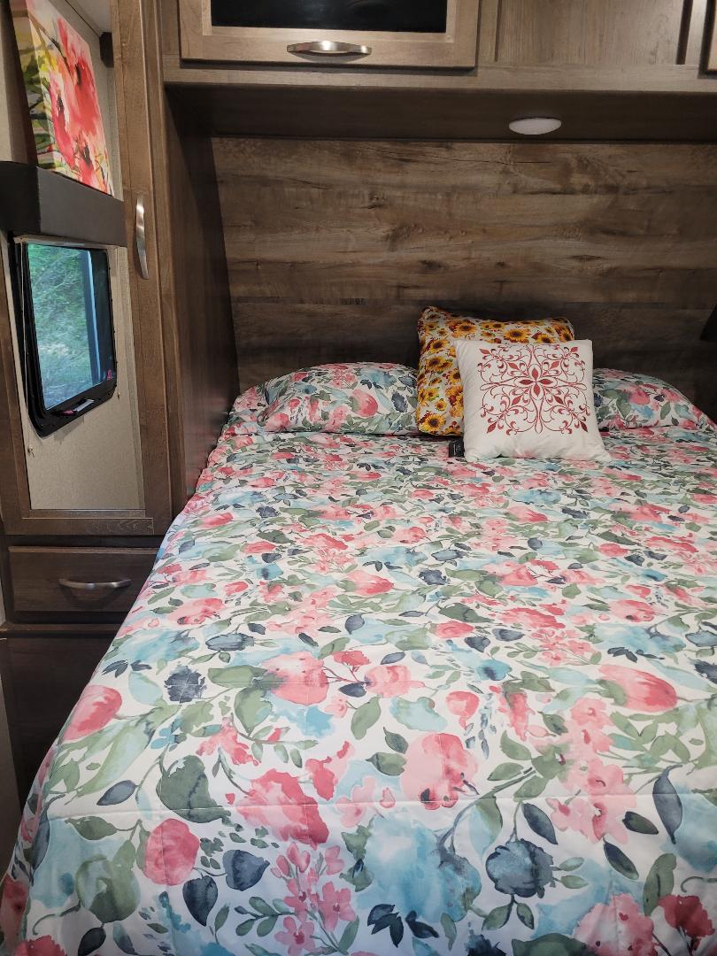 Cozy rv rental bedroom features a bed with vibrant floral bedding, a sunflower pillow, and rustic wood accents.. Dutchmen Coleman 2019