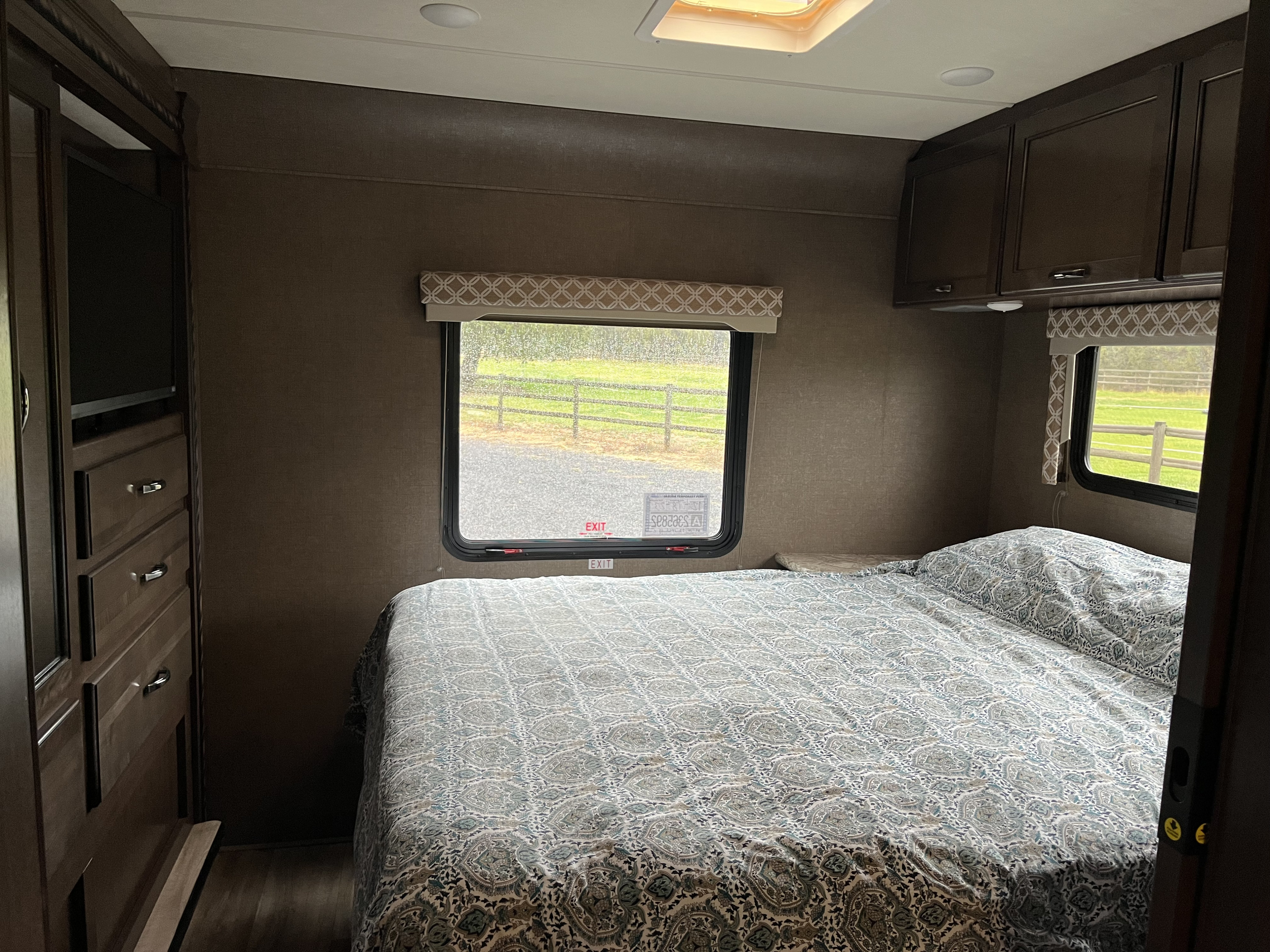 Inside an RV rental, a comfy bedroom features a patterned bed, built-in cabinets, and a window with a green field view.. Thor Freedom Elite 2018