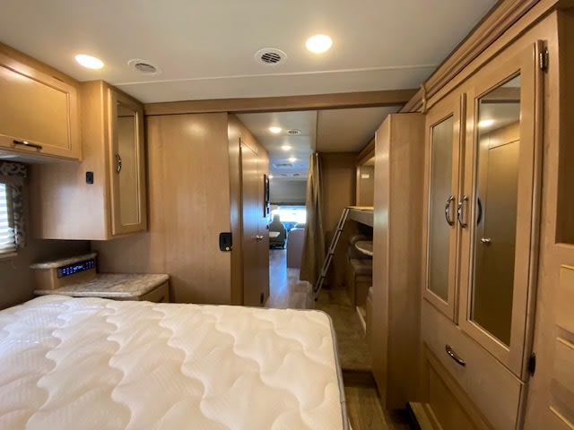 Spacious RV rental interior: bedroom with mattress, cabinets, and hallway leading to bunk beds. Ideal for family adventures.. Thor Motor Coach Four Winds 2020