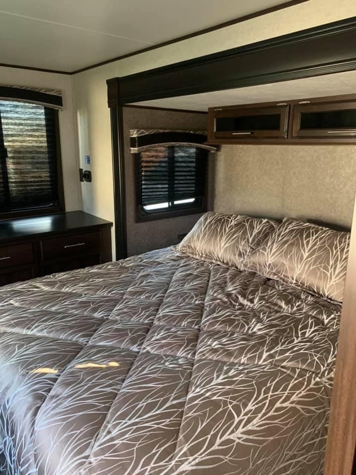 Cozy RV rental bedroom featuring a comfortable bed with patterned bedding, overhead cabinets, and dual windows with blinds.. Jayco Jay Flight 2019
