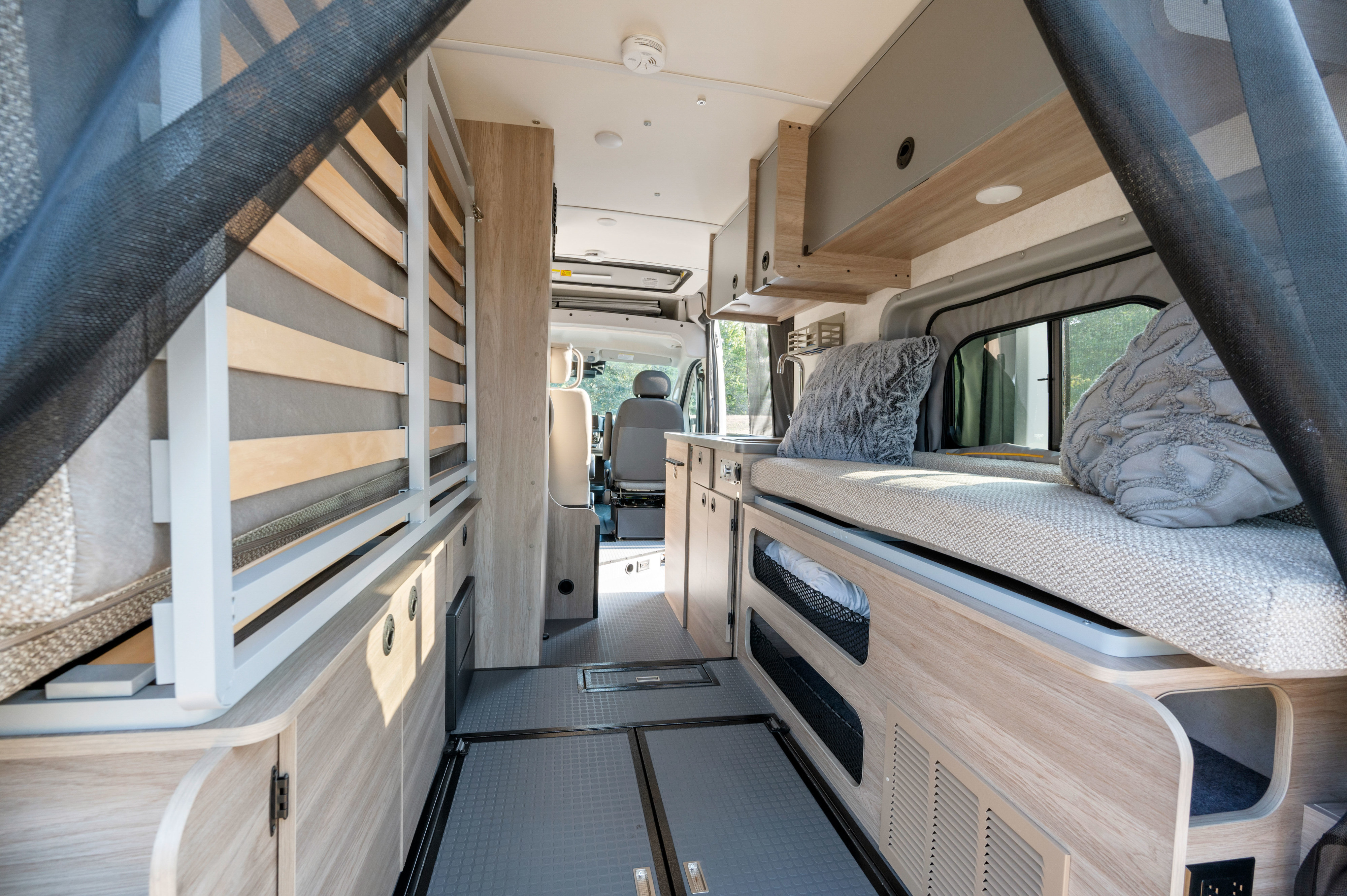 Bright RV rental interior showing a flexible bed system, kitchen counter, and storage, perfect for your next road trip.. Winnebago Solis 2023