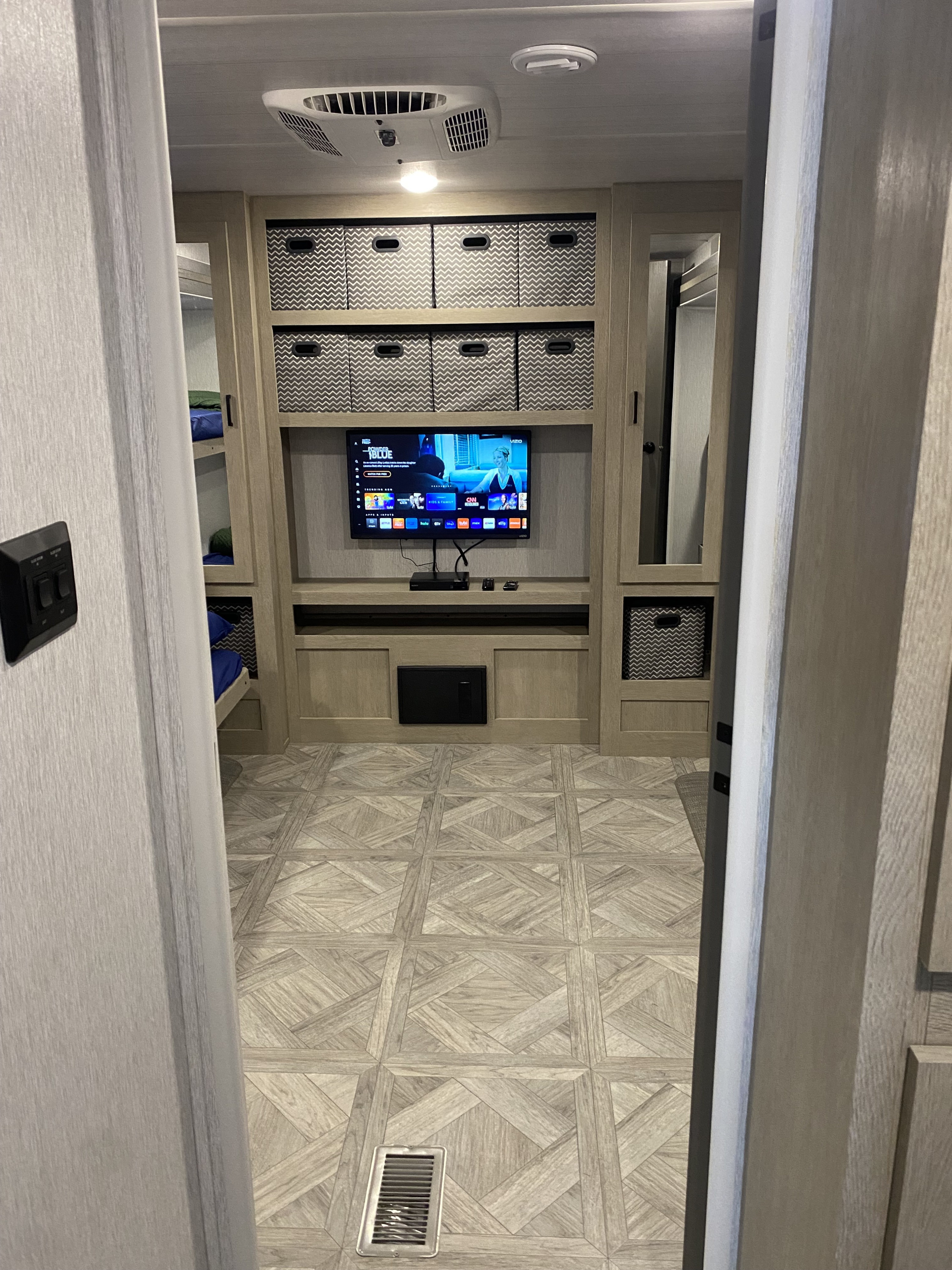 Spacious and modern RV rental interior with entertainment area, chevron storage bins, bunk beds, and AC unit.. Forest River Wildwood 2023