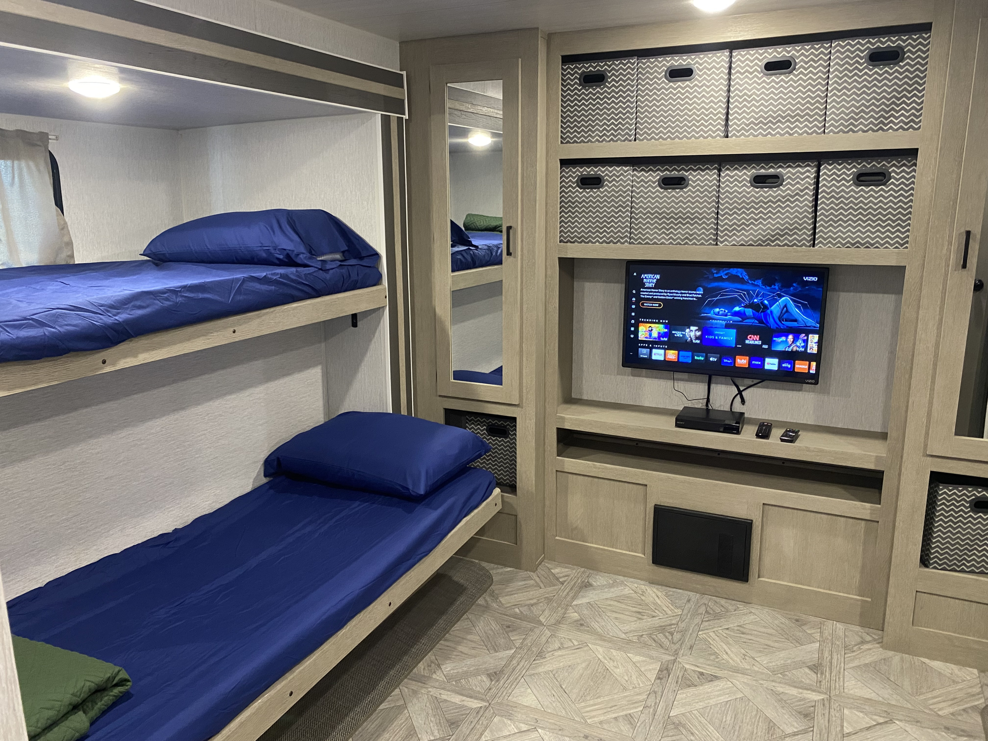 RV rental bunk room: comfy beds, TV, and organized storage shelves. Perfect for family camping trips.. Forest River Wildwood 2023