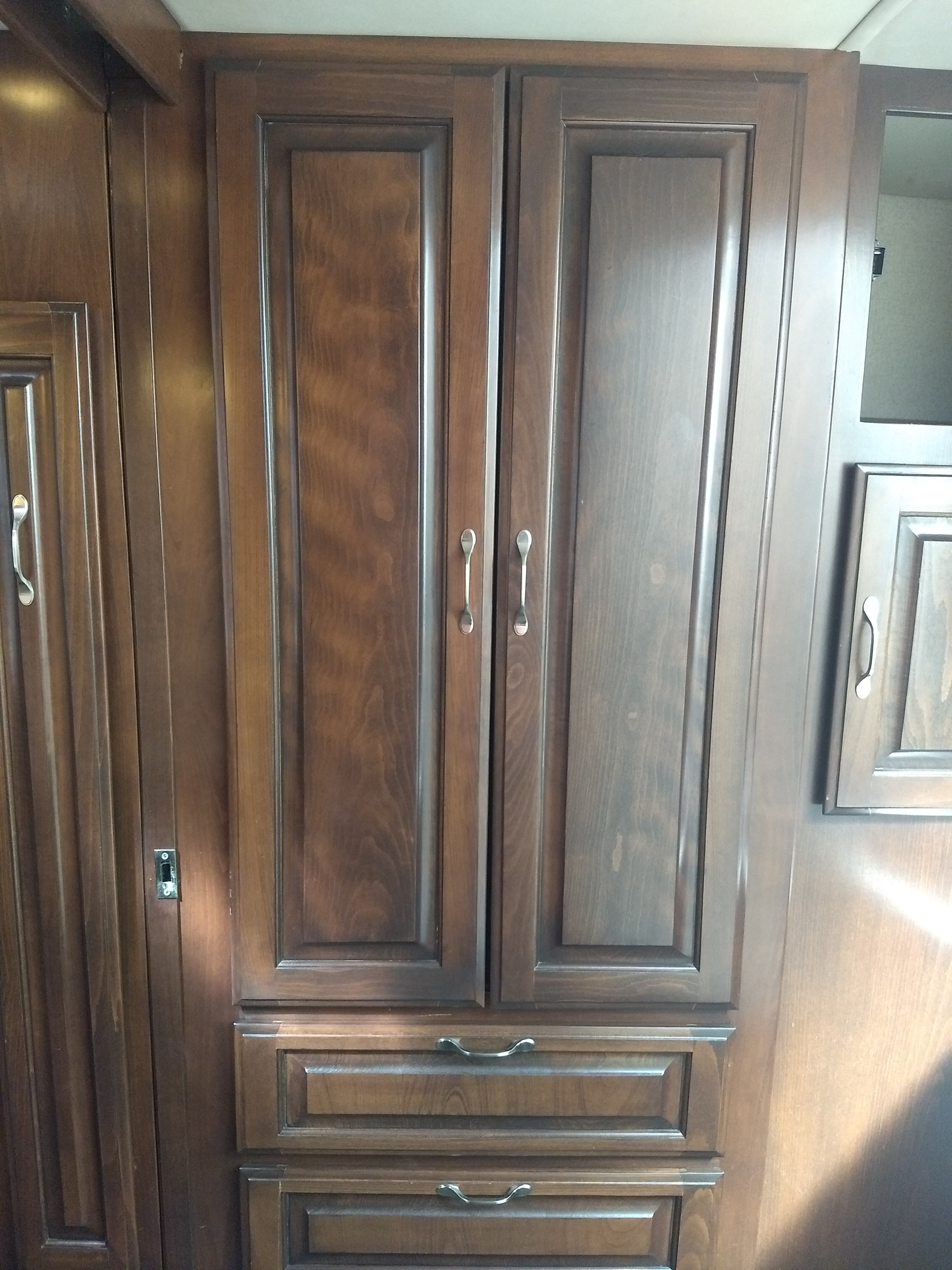Dark wood cabinetry with doors and drawers, featuring silver handles, for a comfortable RV rental interior.. Regency Conversions Ultra Brougham 2019