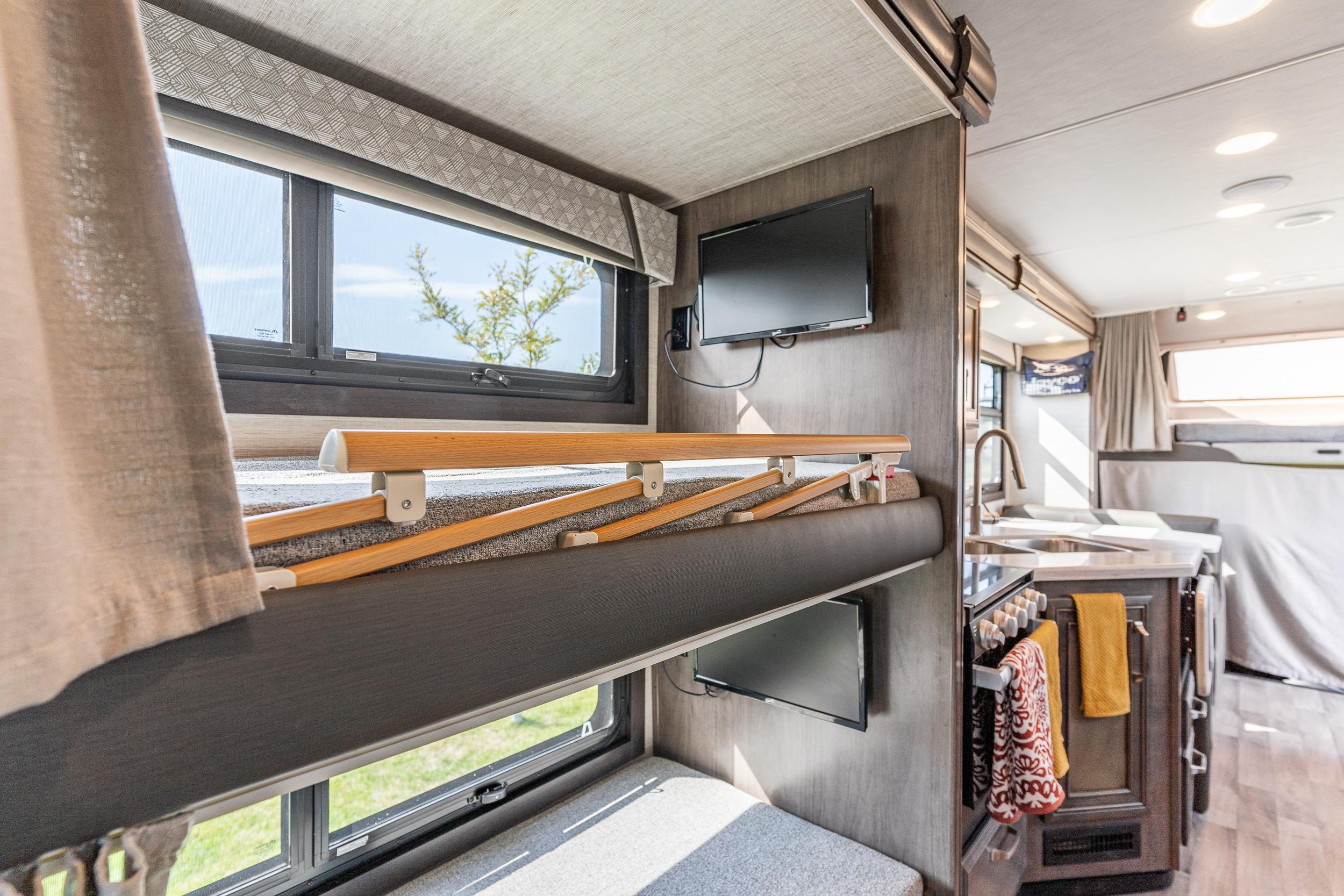 Inside an RV rental, featuring comfortable bunk beds with safety rails, TVs, and a compact kitchen.. Jayco Greyhawk Prestige 2022