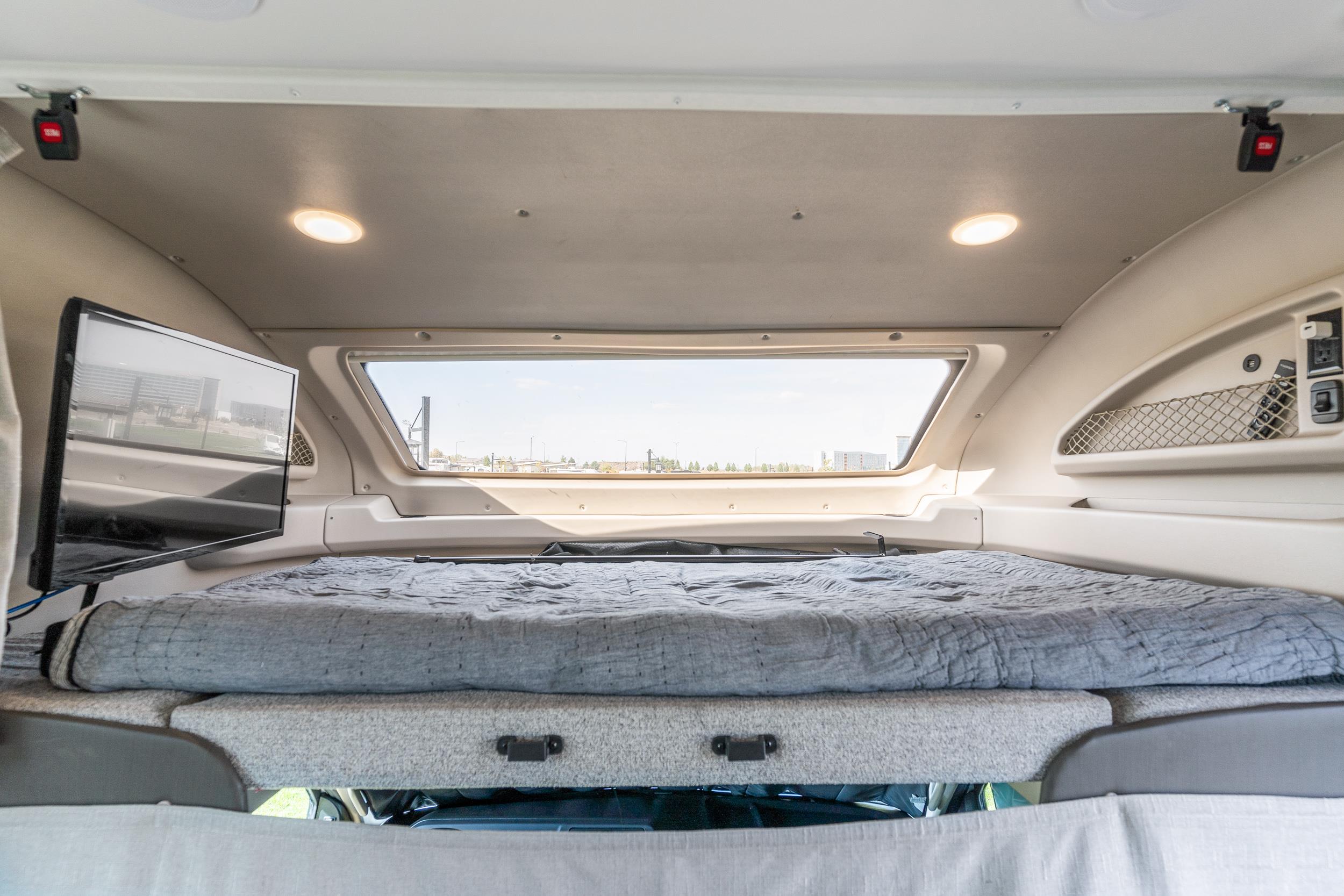 RV rental's cozy cab-over bed with window, mounted TV, and integrated power outlets/storage for comfort.. Jayco Greyhawk Prestige 2022