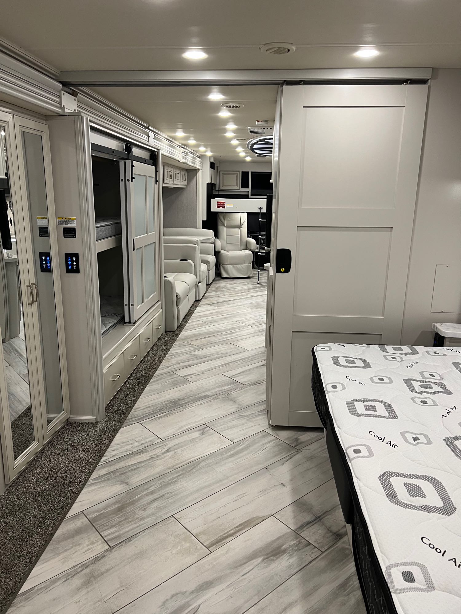 Bright RV rental interior: view from a bedroom past sliding doors to bunk beds, a long hallway, and comfortable recliners.. Fleetwood Discovery 2022