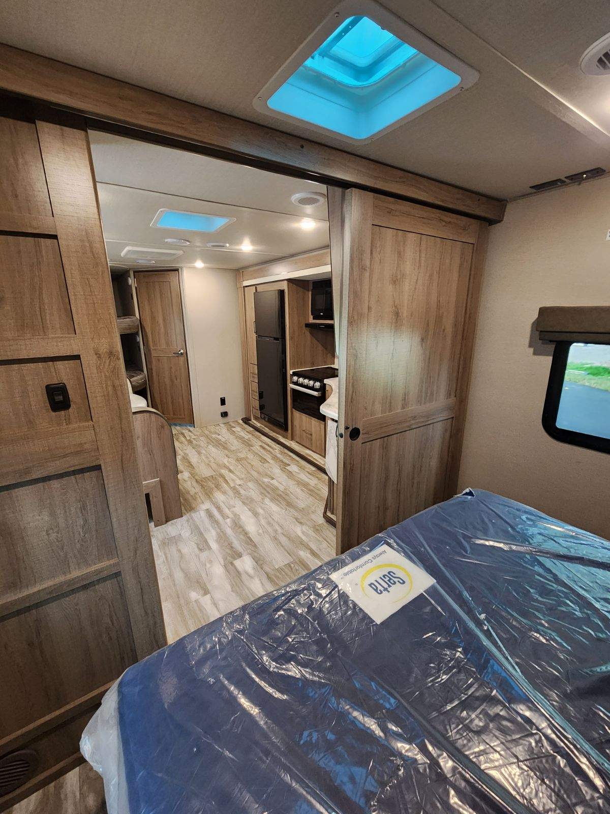 RV rental interior: A bright, spacious view of the kitchen, bed, and living area, featuring wood cabinetry and skylights.. Grand Design Imagine 2022
