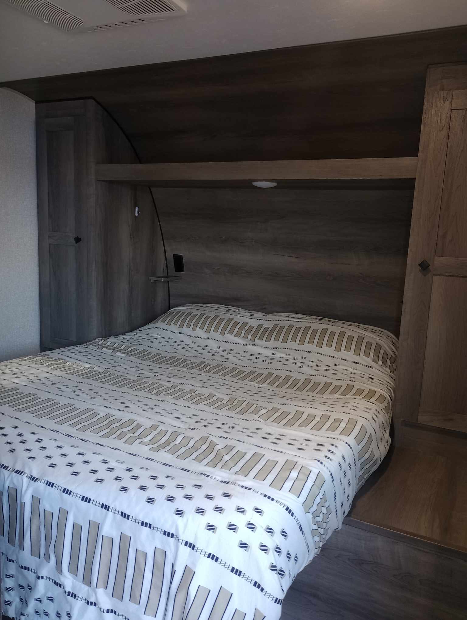 Inside a comfortable RV rental bedroom featuring a striped bed, built-in wooden cabinets, and an overhead shelf.. KZ Sportsmen SE 312BHKSE (Delivery Only) 2021