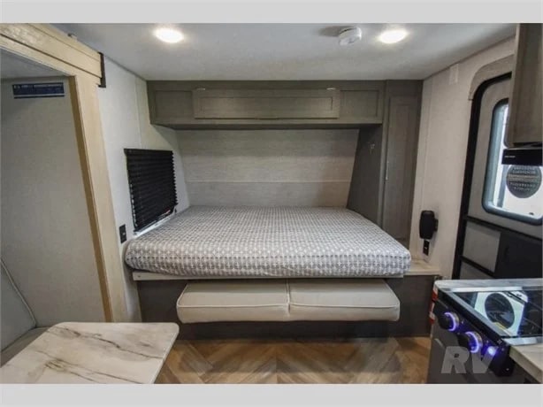 This compact RV rental interior features a comfortable bed, overhead storage, and a functional kitchen area, ideal for adventurers.. Ozark Ascent 2023