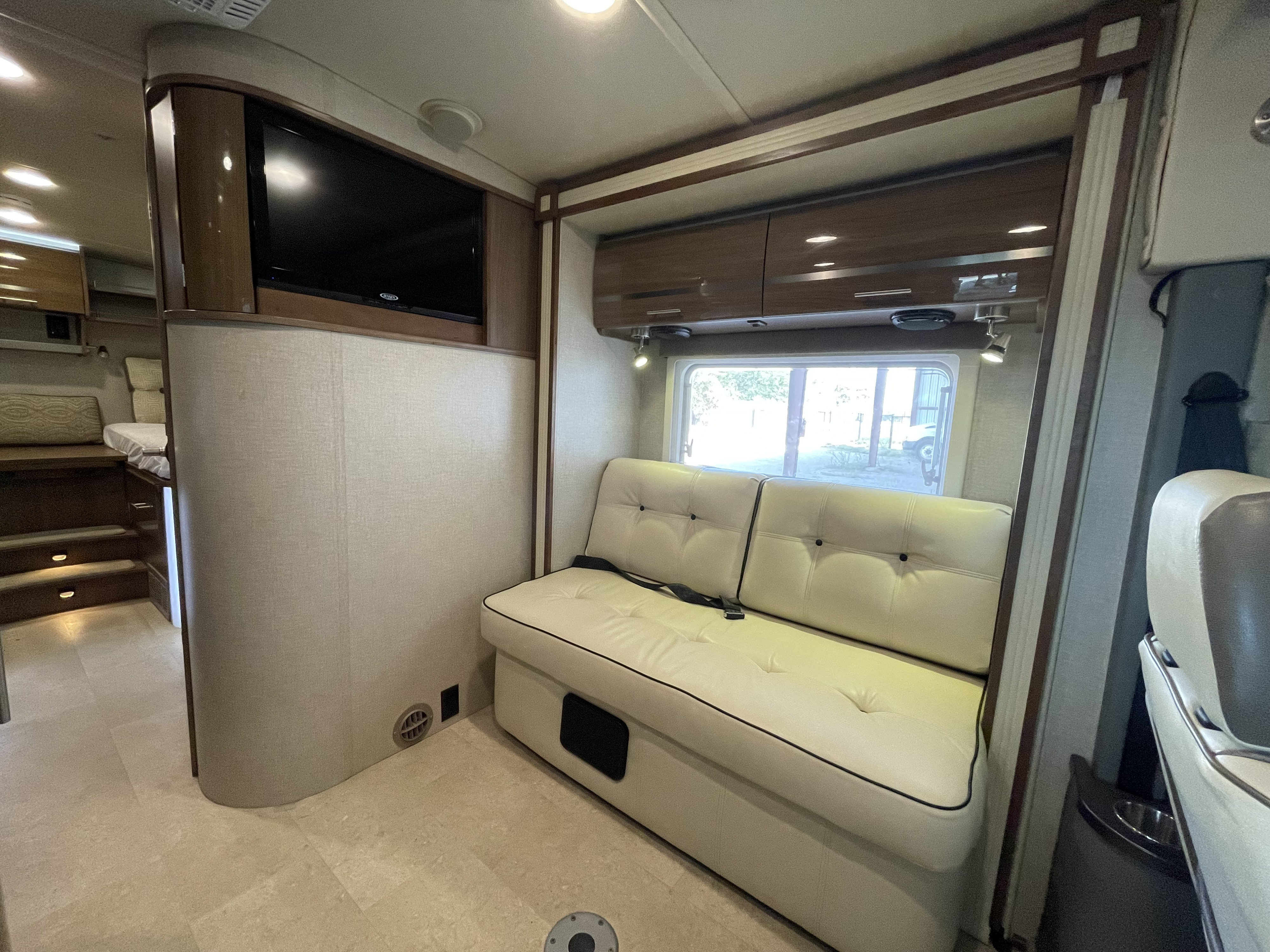 Modern rv rental interior showing a cream couch, TV, and bed area. Comfortable living on the road.. Winnebago Via 2015
