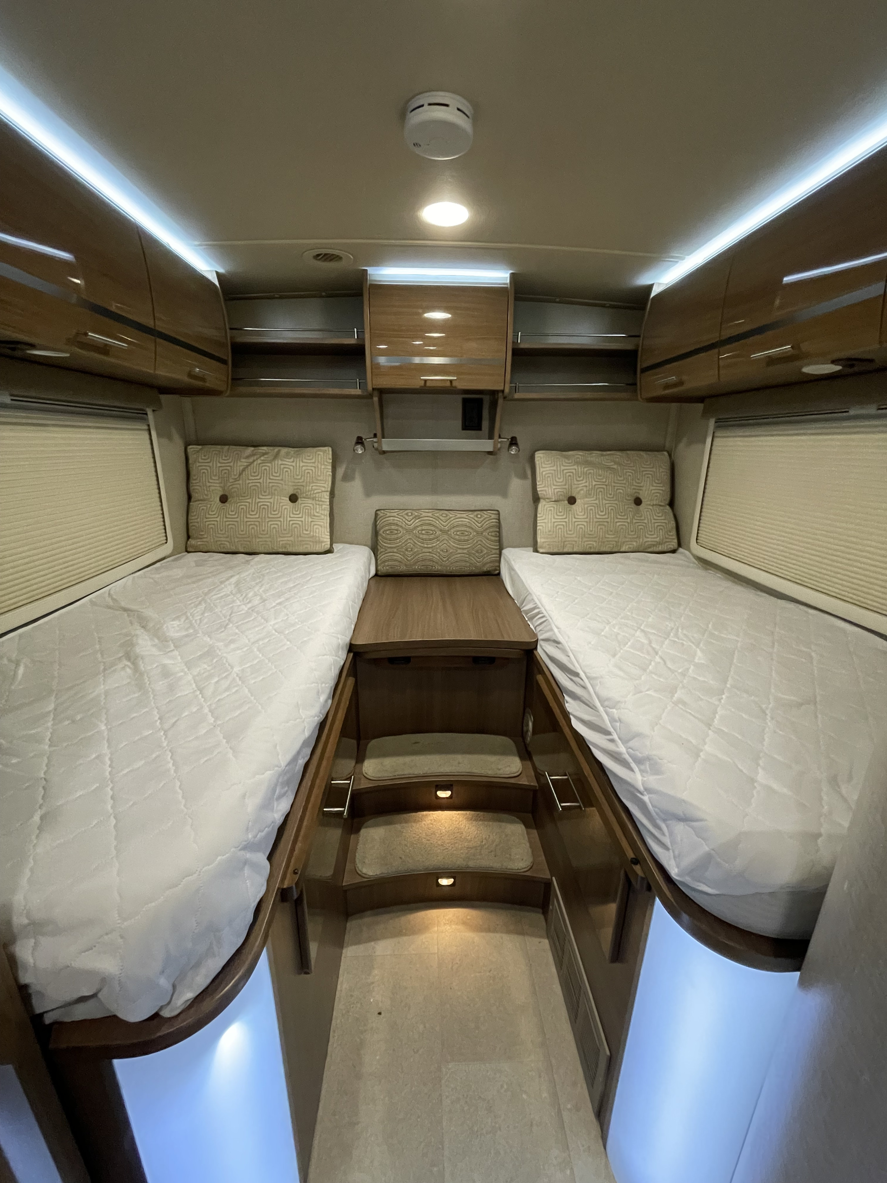 Spacious RV rental bedroom featuring two comfortable beds, overhead storage, steps, and ambient lighting for travel comfort.. Winnebago Via 2015