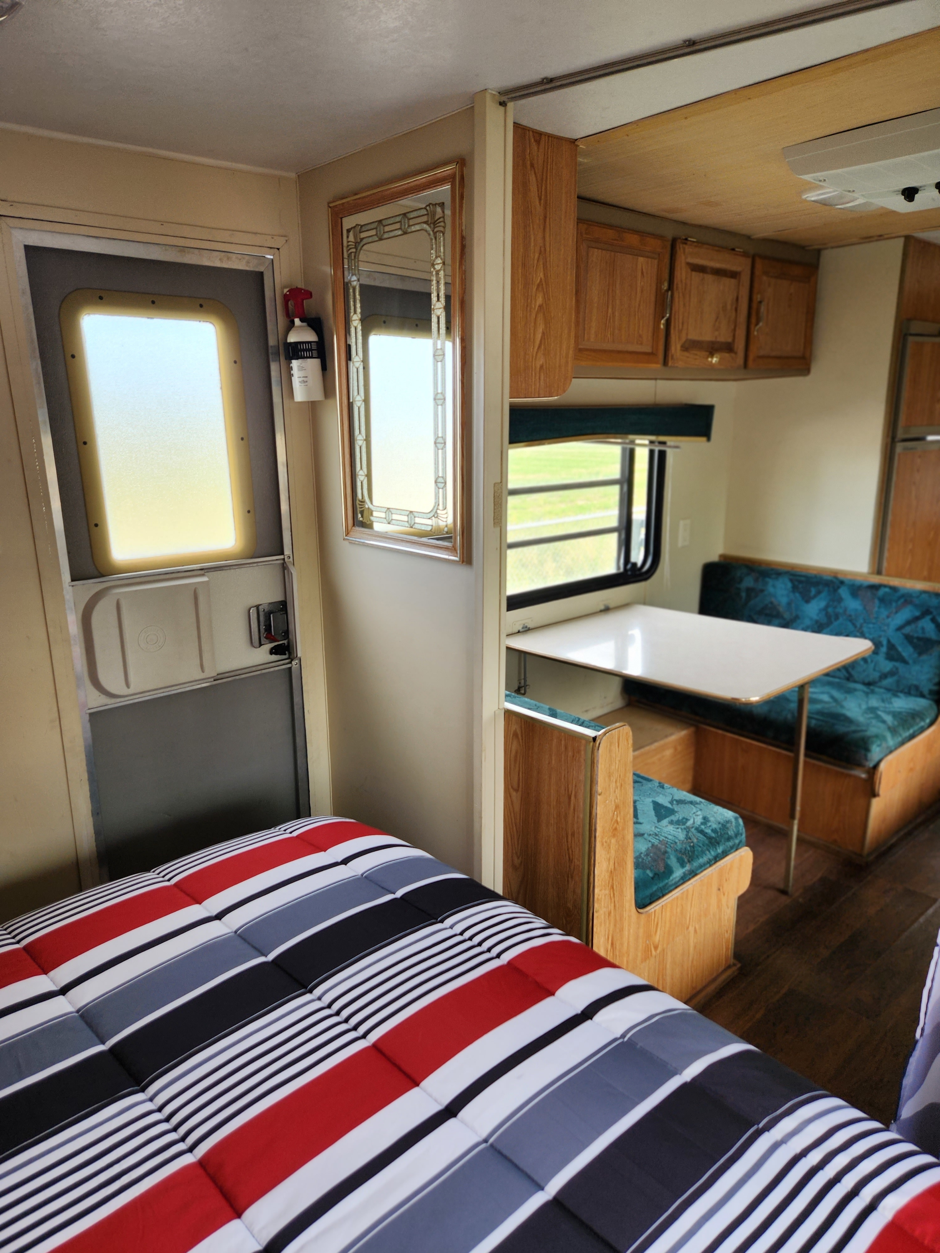 Cozy RV rental interior showcasing a comfy striped bed, dinette with teal seating, and functional cabinets.. Skyline Layton 1995