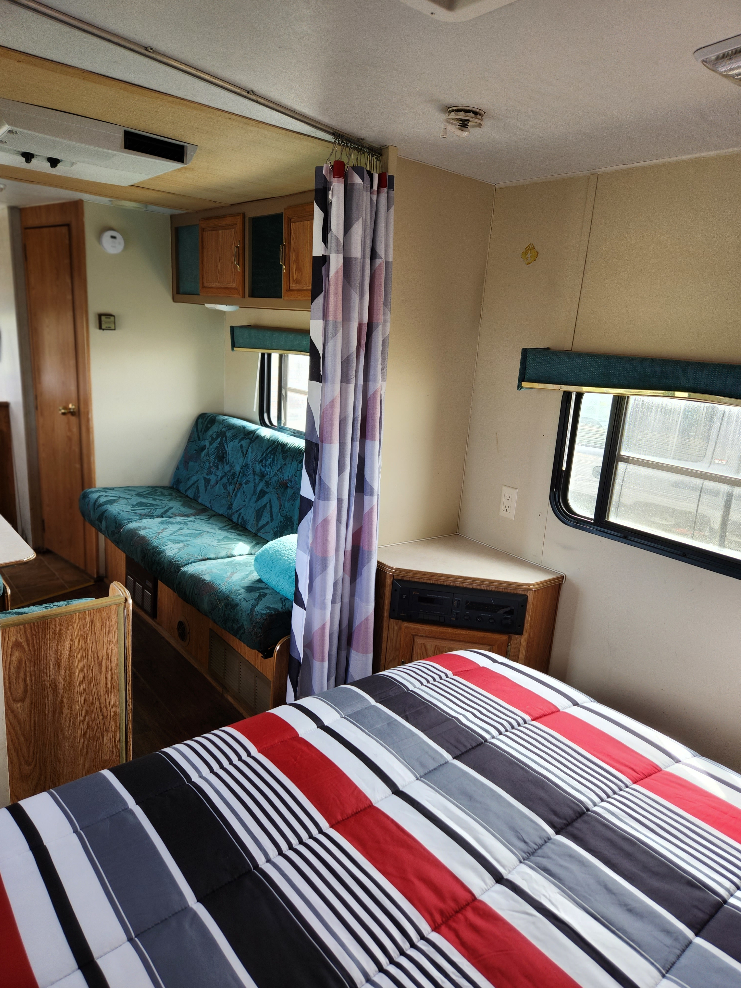 Inside an RV rental: a comfortable bedroom area with a striped comforter and an adjacent teal dinette.. Skyline Layton 1995