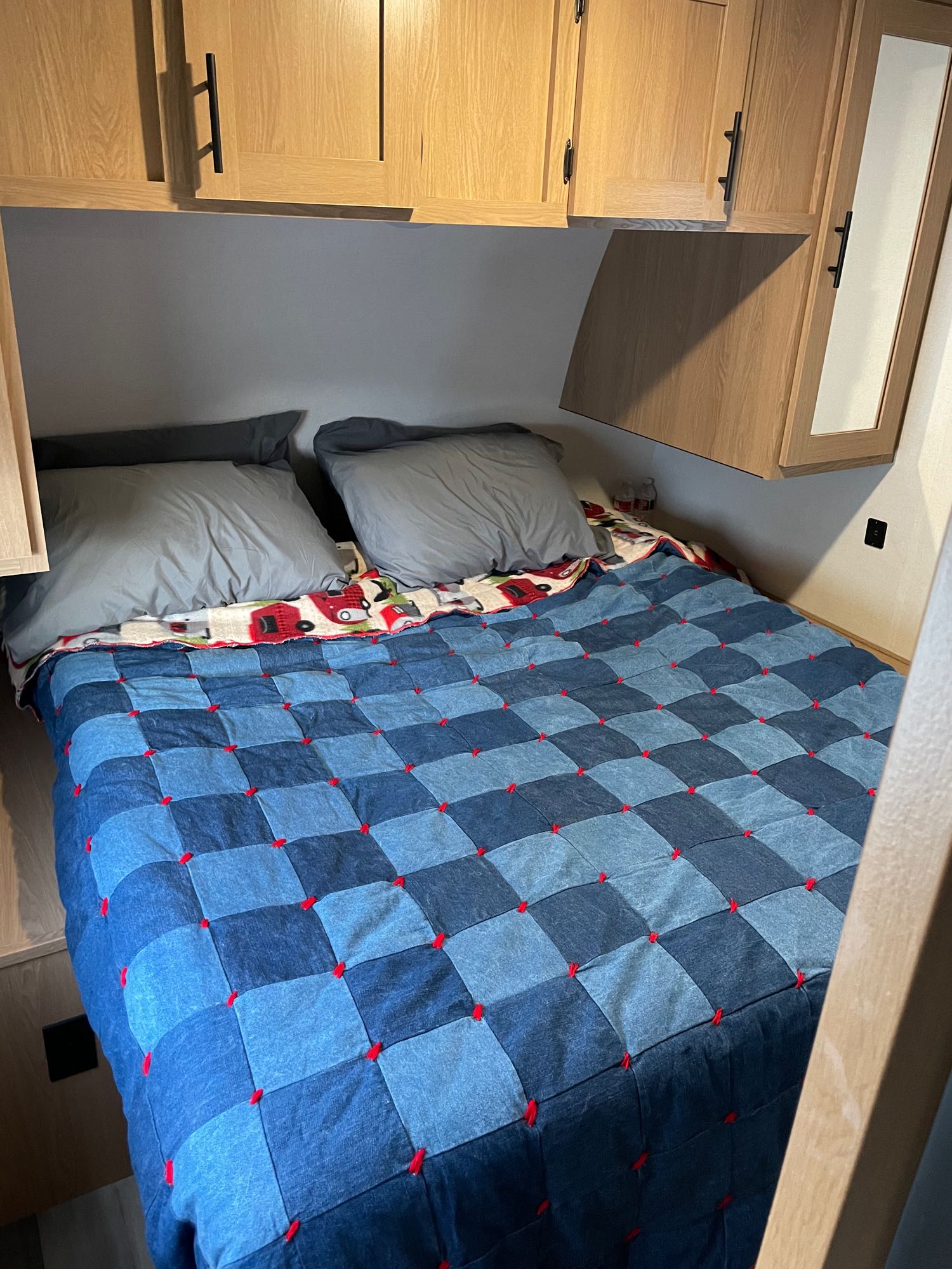 Cozy RV rental bedroom with a blue denim quilt over a truck-patterned blanket. Features wood cabinets overhead.. Avenger Avenger Trailer 2022