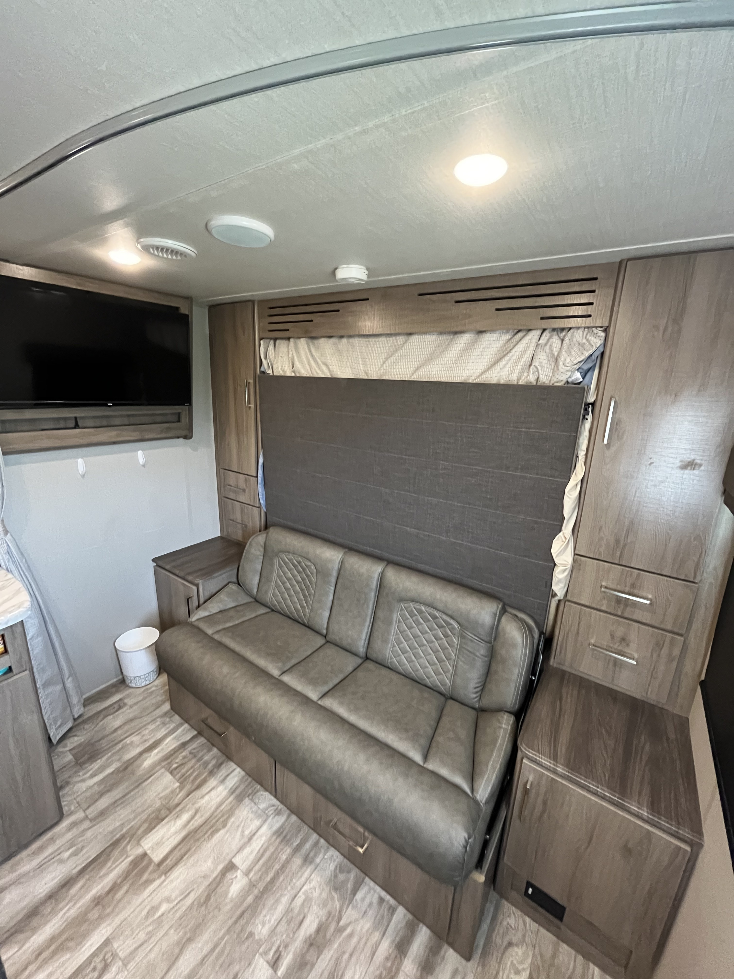 Multi-functional RV rental interior with a gray sofa converting to a bed, wall TV, and clever storage solutions.. Grand Design Imagine 2021