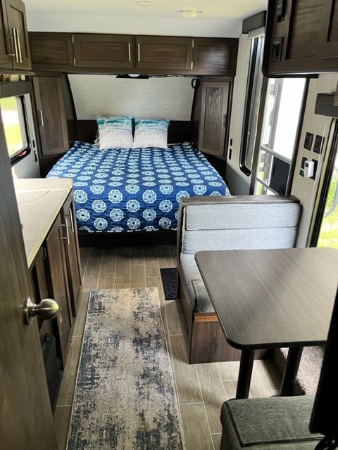 Inside this RV rental: a cozy bedroom with blue bedding, a dinette, and a kitchen area, all with dark wood details.. Forest River Cherokee Wolf Pup 2020
