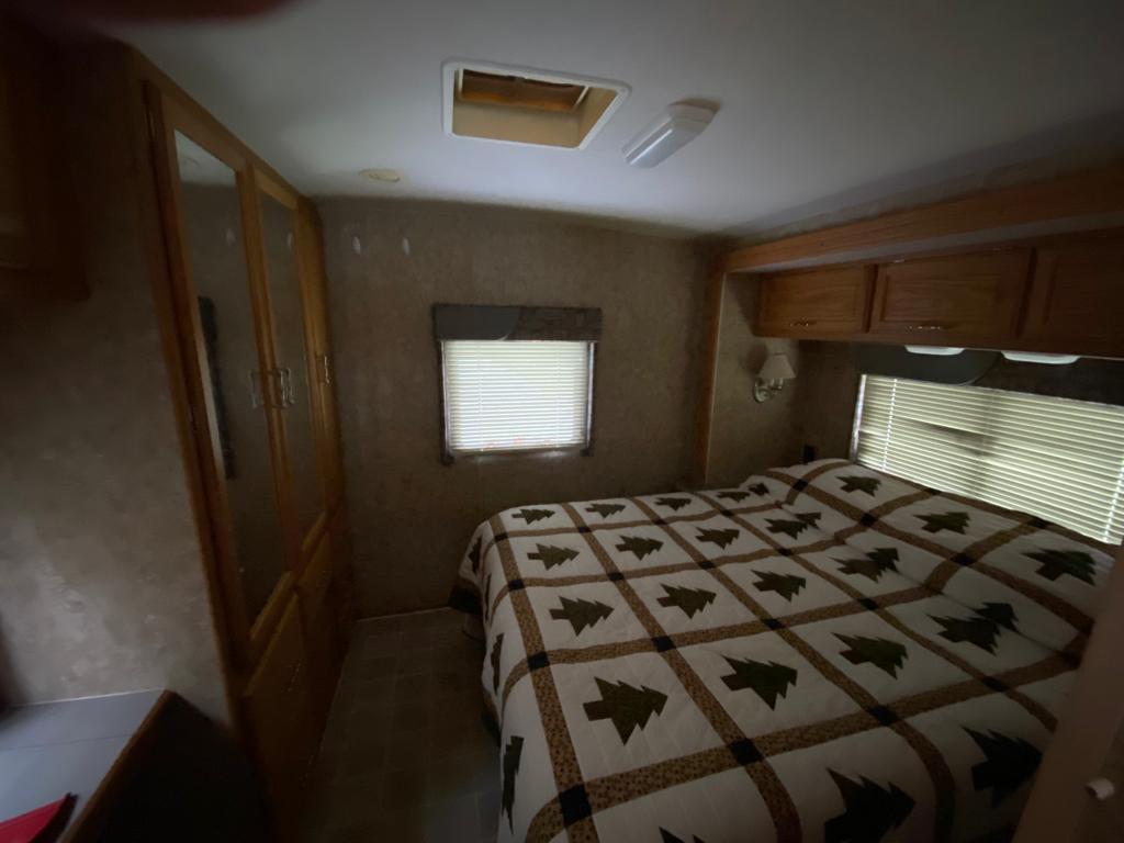 Cozy RV rental bedroom with a tree-patterned bed, windows, and wood storage, perfect for your next adventure.. Winnebago Chalet 2007