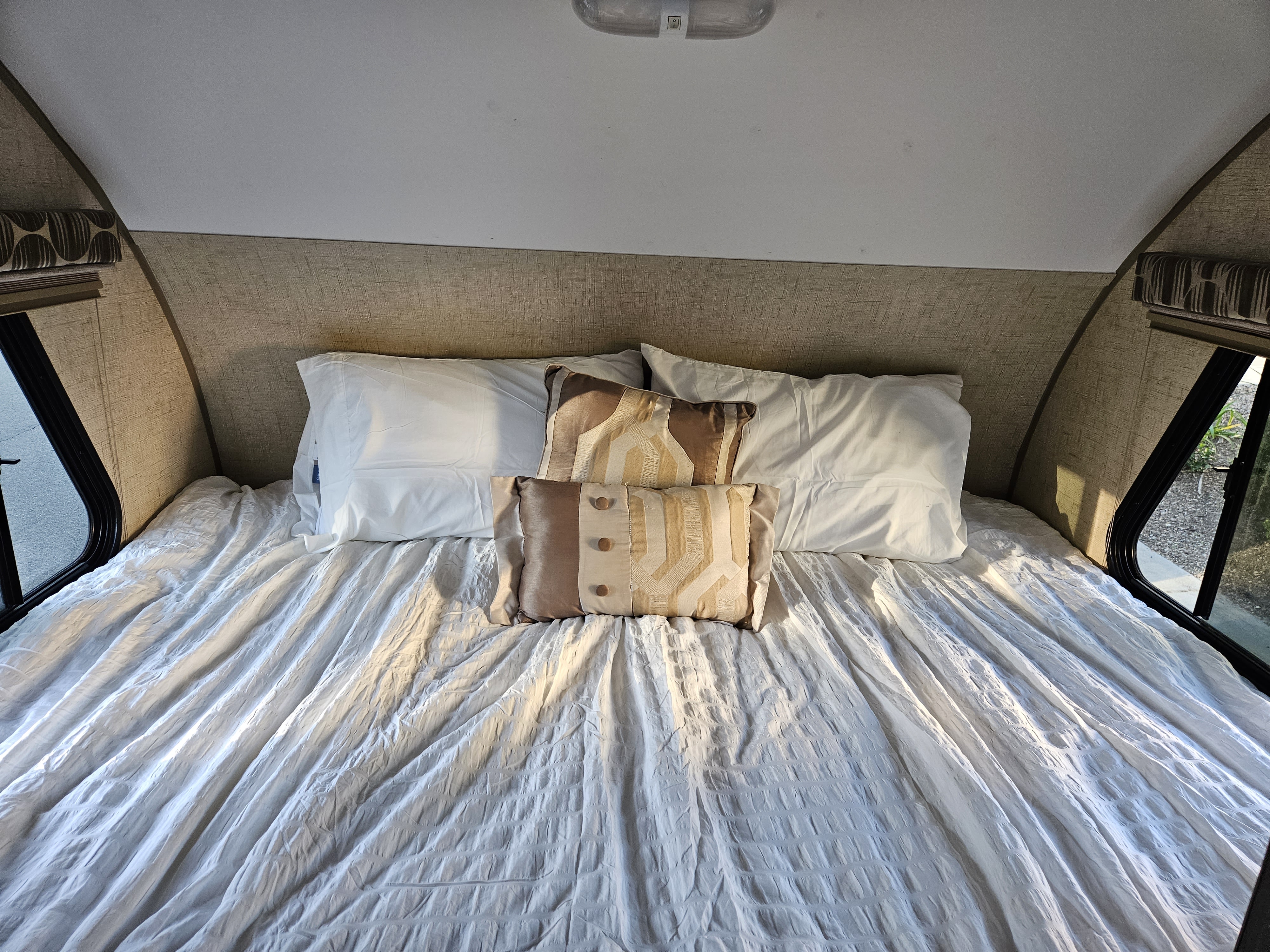 Comfortable RV rental bedroom with a full bed, white sheets, and decorative pillows. Natural light streams through the windows.. Forest River Rpod 179 2015