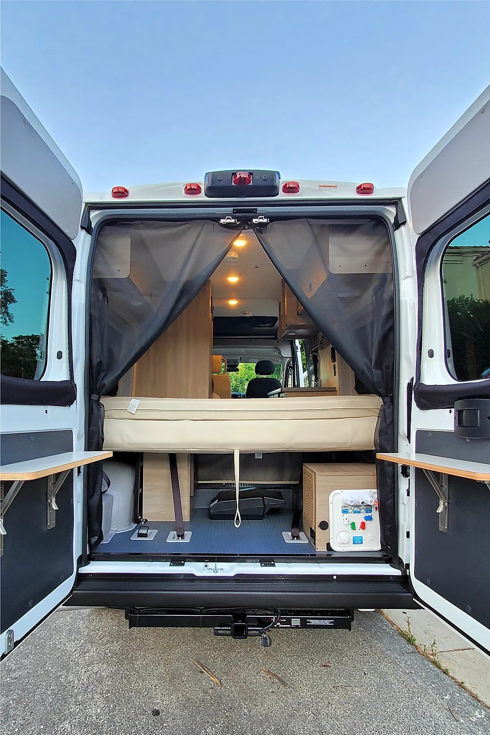 Open RV rental rear view: a cozy bed, accessible storage, and utility panel visible through wide-open doors.. Winnebago Solis 2023