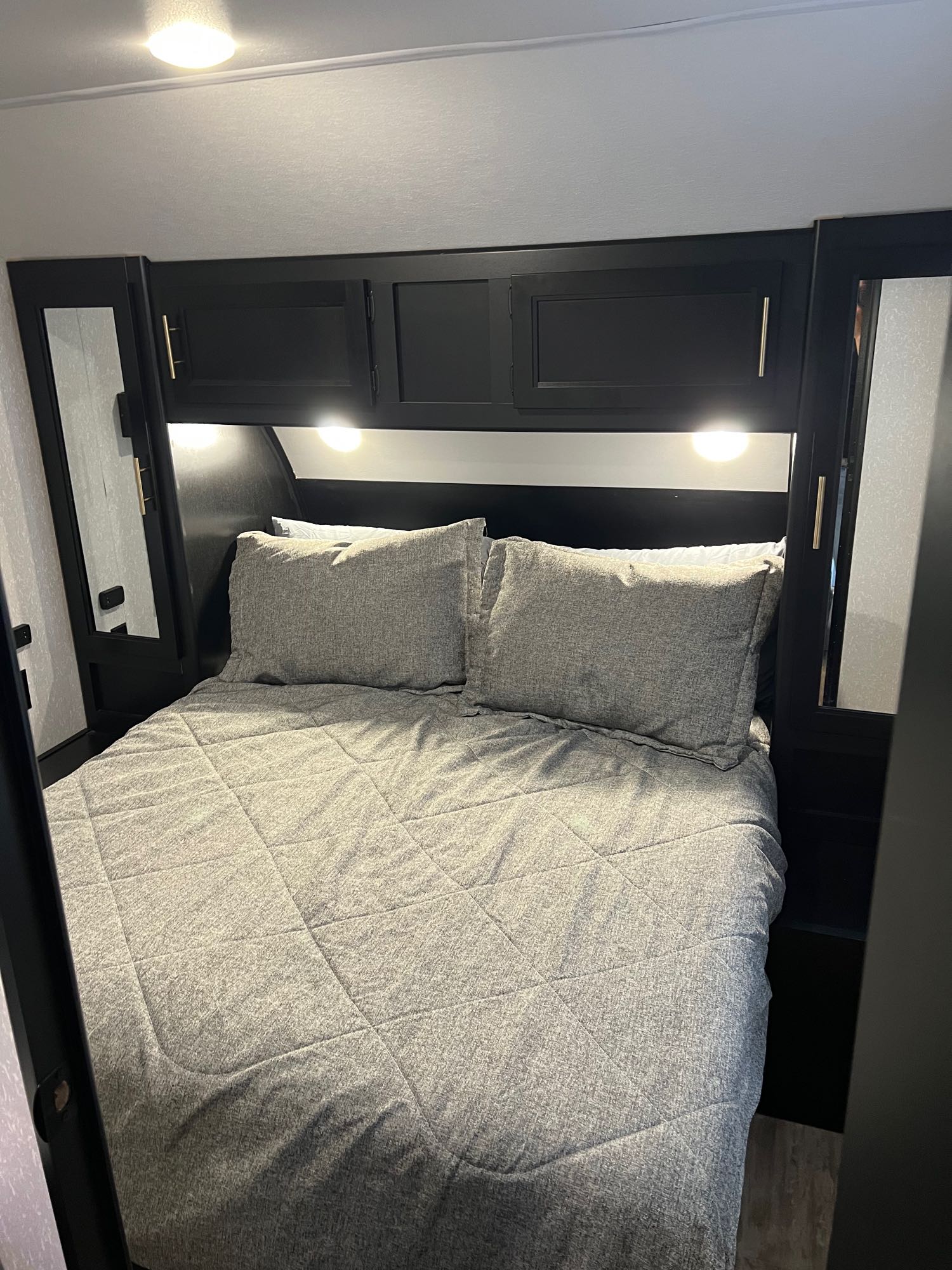Cozy RV rental bedroom with a comfortable gray bed, overhead black cabinets, and integrated reading lights for a relaxing stay.. Forest River Cherokee Cherokee Black Label 2022