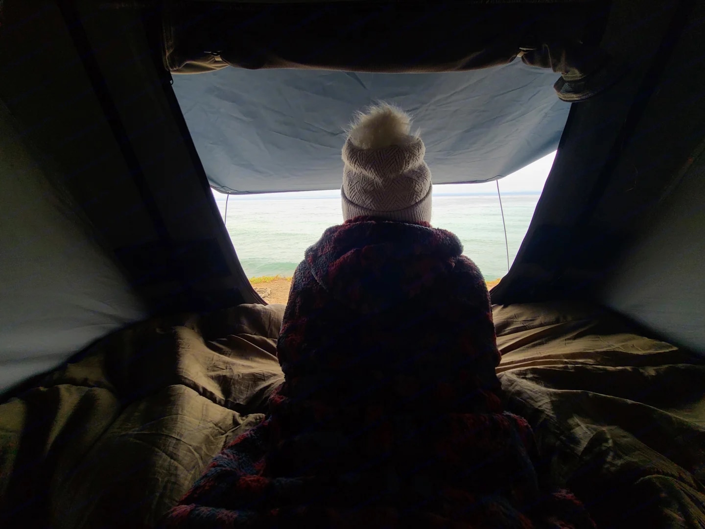Inside an RV rental, a person in a hat faces away, looking out at the vast ocean and coastline from a cozy bed.. Toyota RAV4 2003