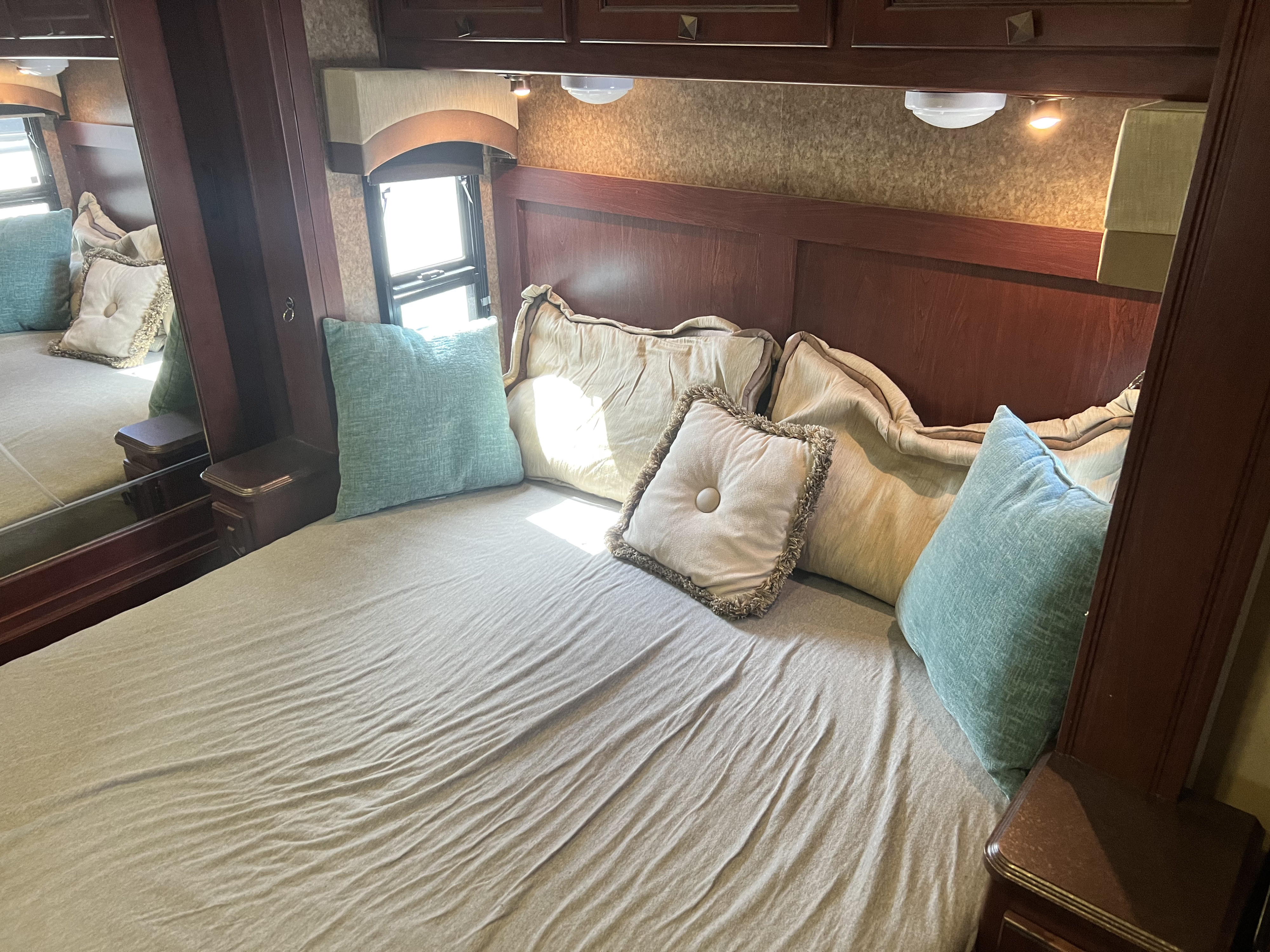 Inside an RV rental: a cozy bedroom featuring a comfortable bed, assorted pillows, and elegant wooden paneling.. Berkshire Berkshire Motorhome 2013