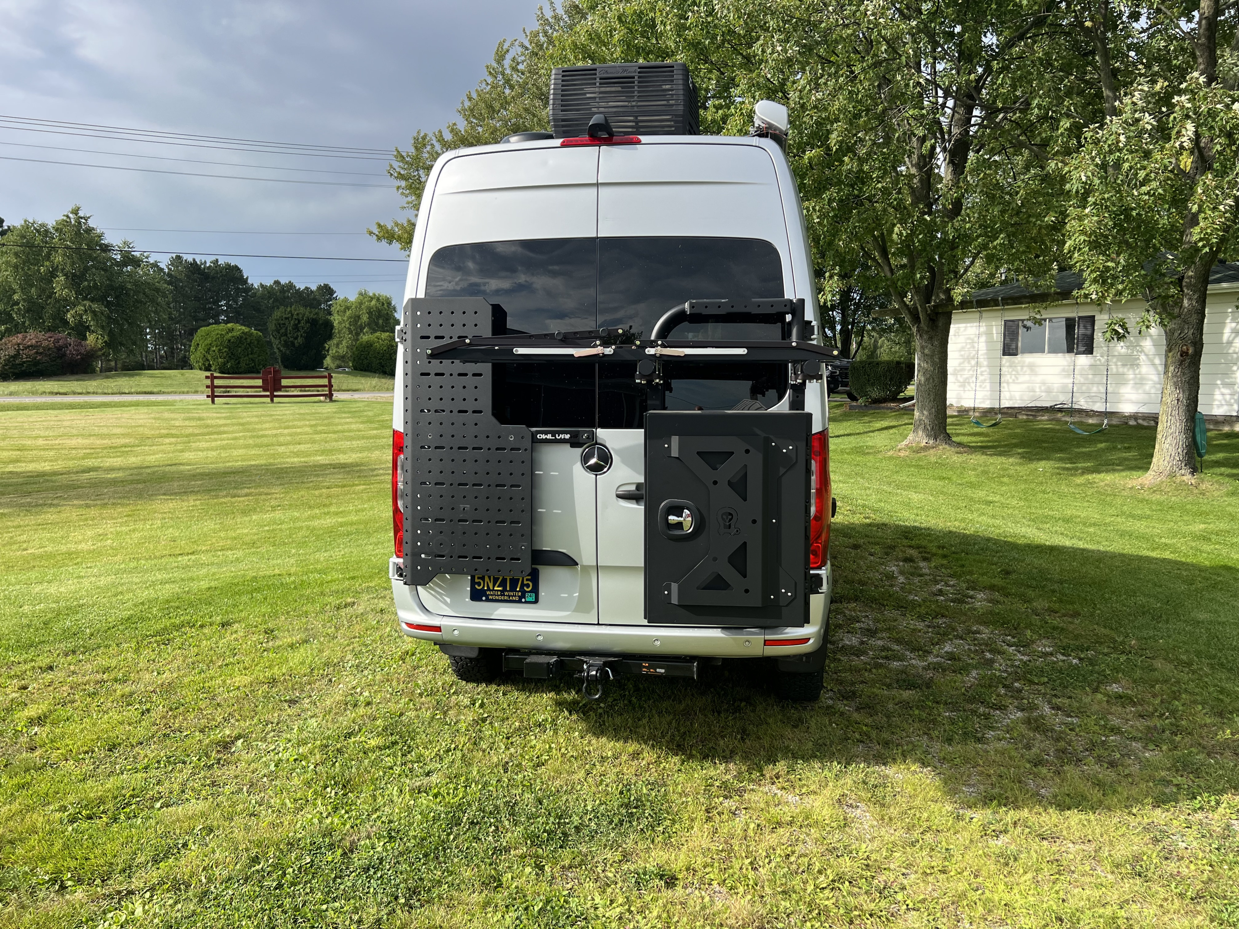 White custom Sprinter van rv rental showcasing rear gear mounts & rooftop AC, parked on a green lawn.. Thor Sanctuary 2023