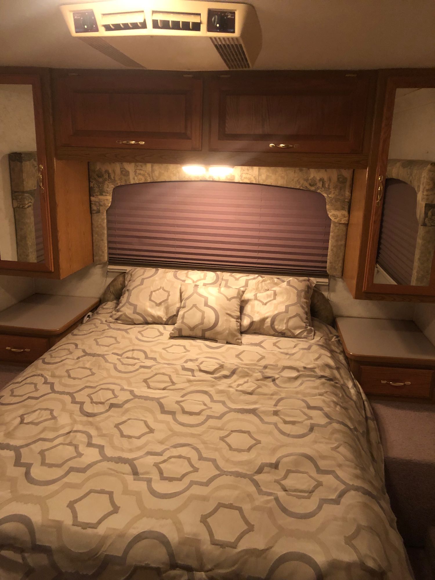 Comfortable RV rental bedroom featuring a patterned bed, overhead storage, and window blinds for a cozy travel experience.. Four Winds Hurricane 2002