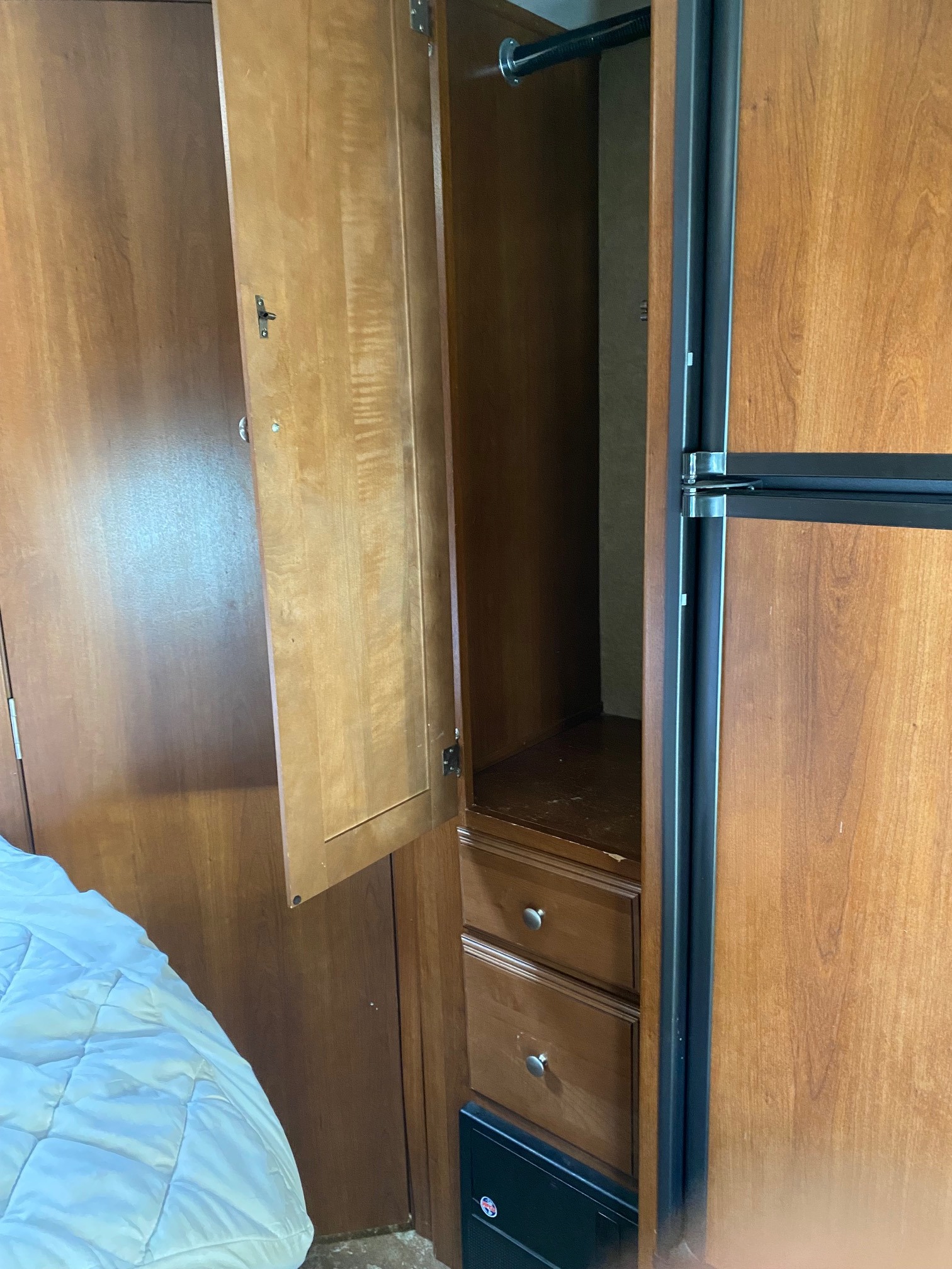 RV rental interior featuring an open wooden wardrobe with a hanging rod, storage drawers, and a built-in refrigerator.. Coachmen Leprechaun 2016