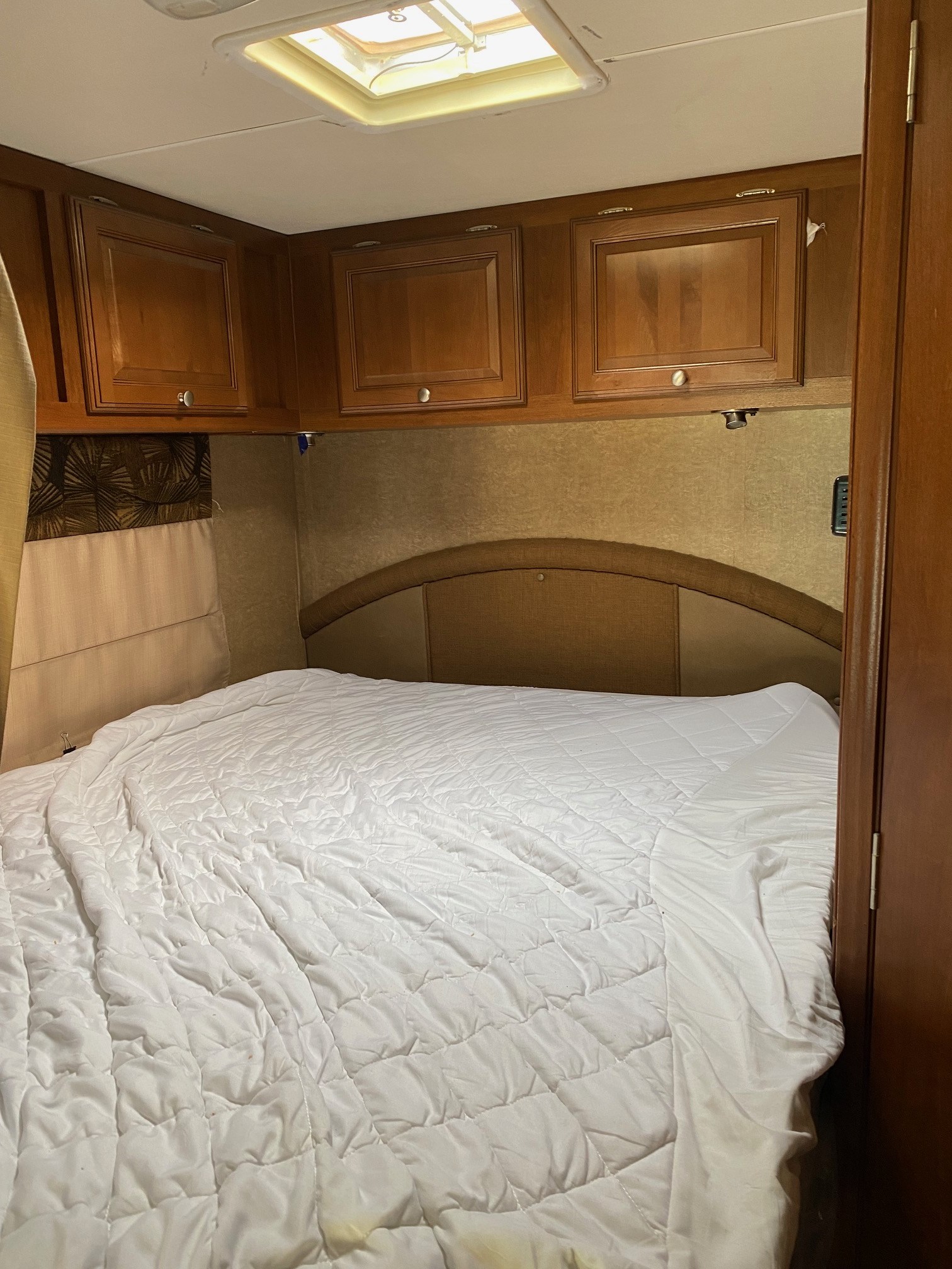 Cozy RV rental bedroom with a comfy bed, white comforter, overhead cabinets, and headboard, ready for your trip.. Coachmen Leprechaun 2016