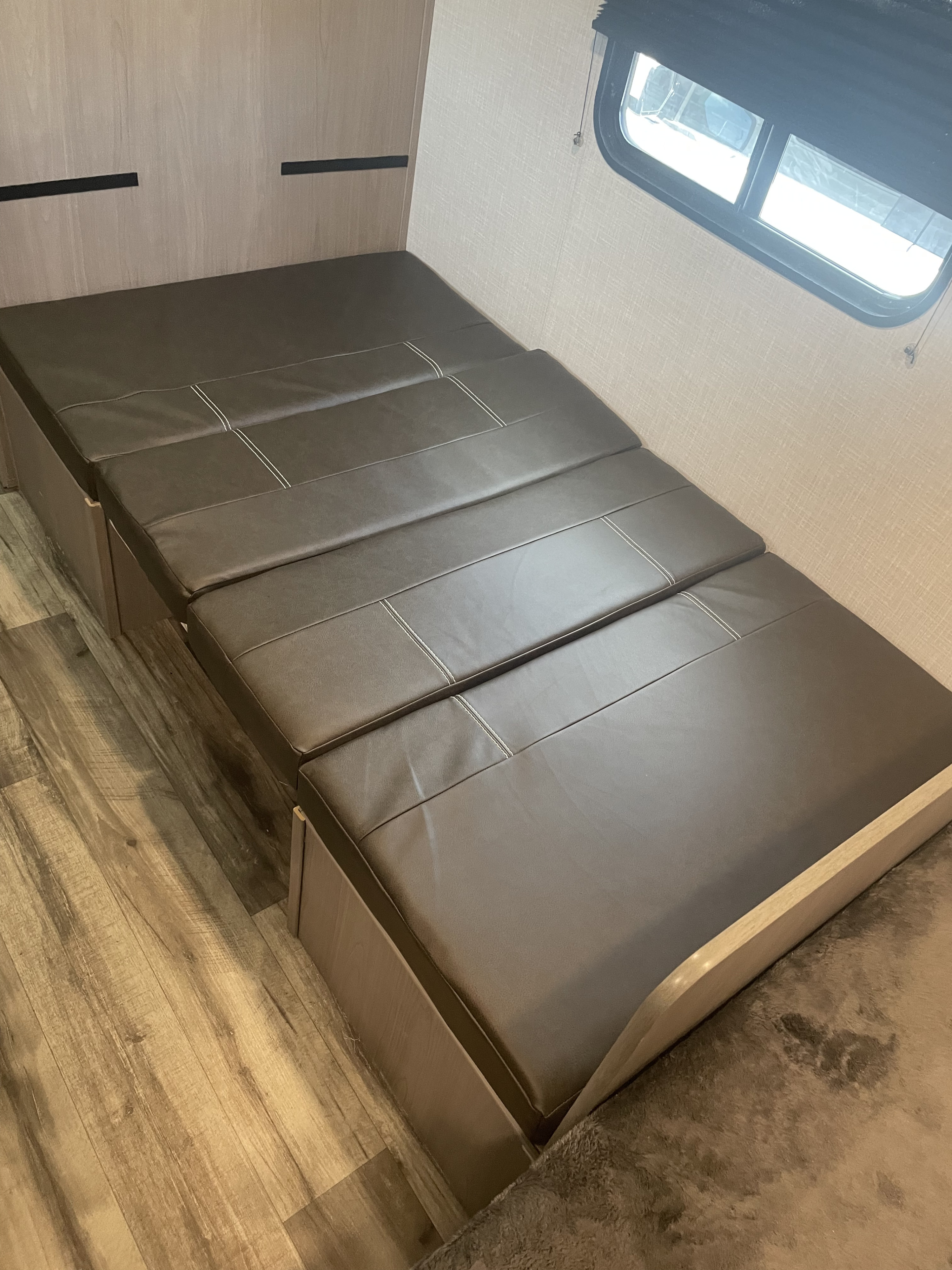 Versatile RV rental interior: A dark brown, multi-section convertible sofa bed, ideal for seating or sleeping, with wood flooring and a window.. Dutchmen Coleman Lantern LT 2023