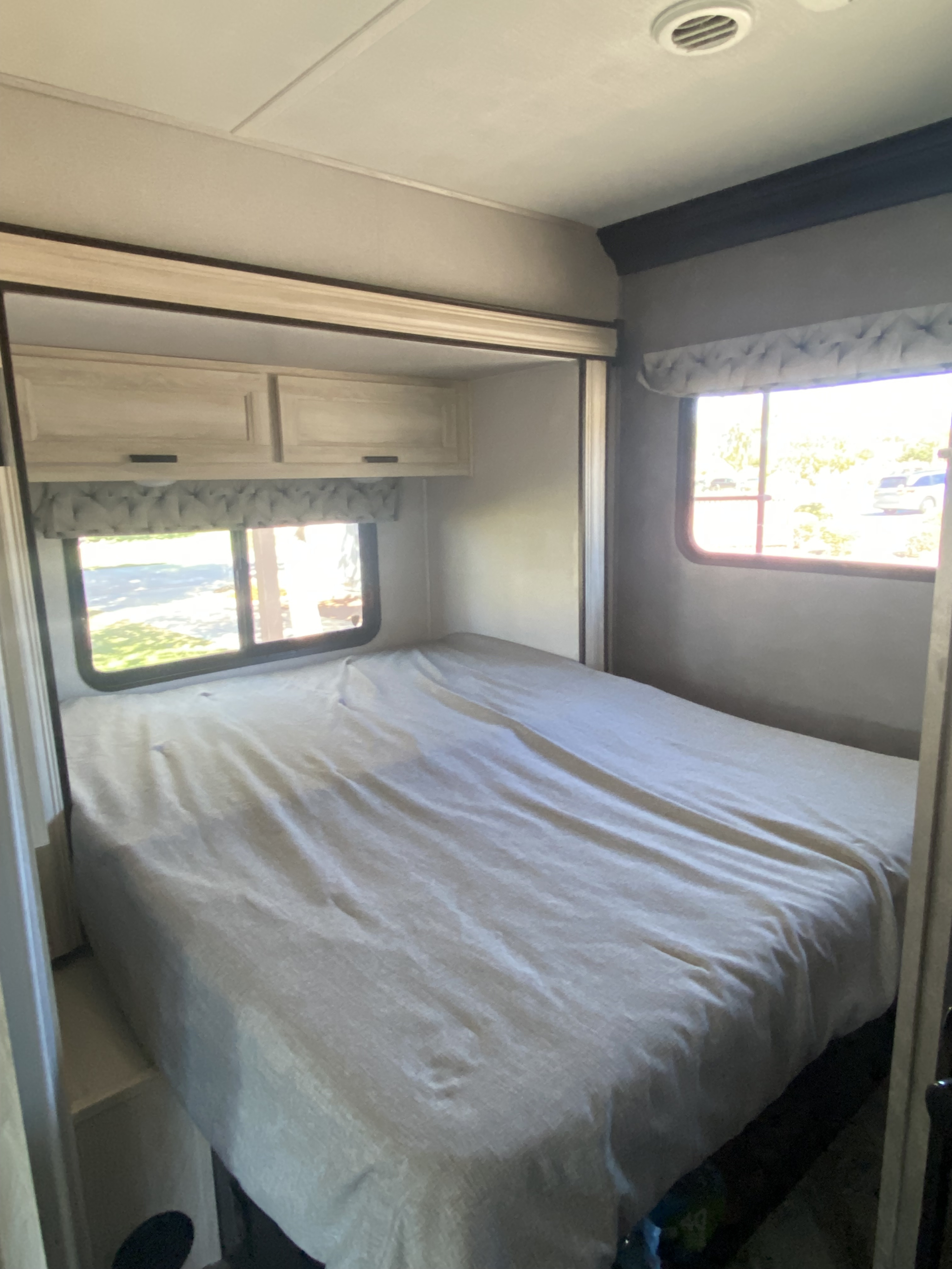 Cozy RV rental bedroom featuring a full bed with light bedding, wooden overhead cabinets, and bright windows on both sides.. Forester LE 2021