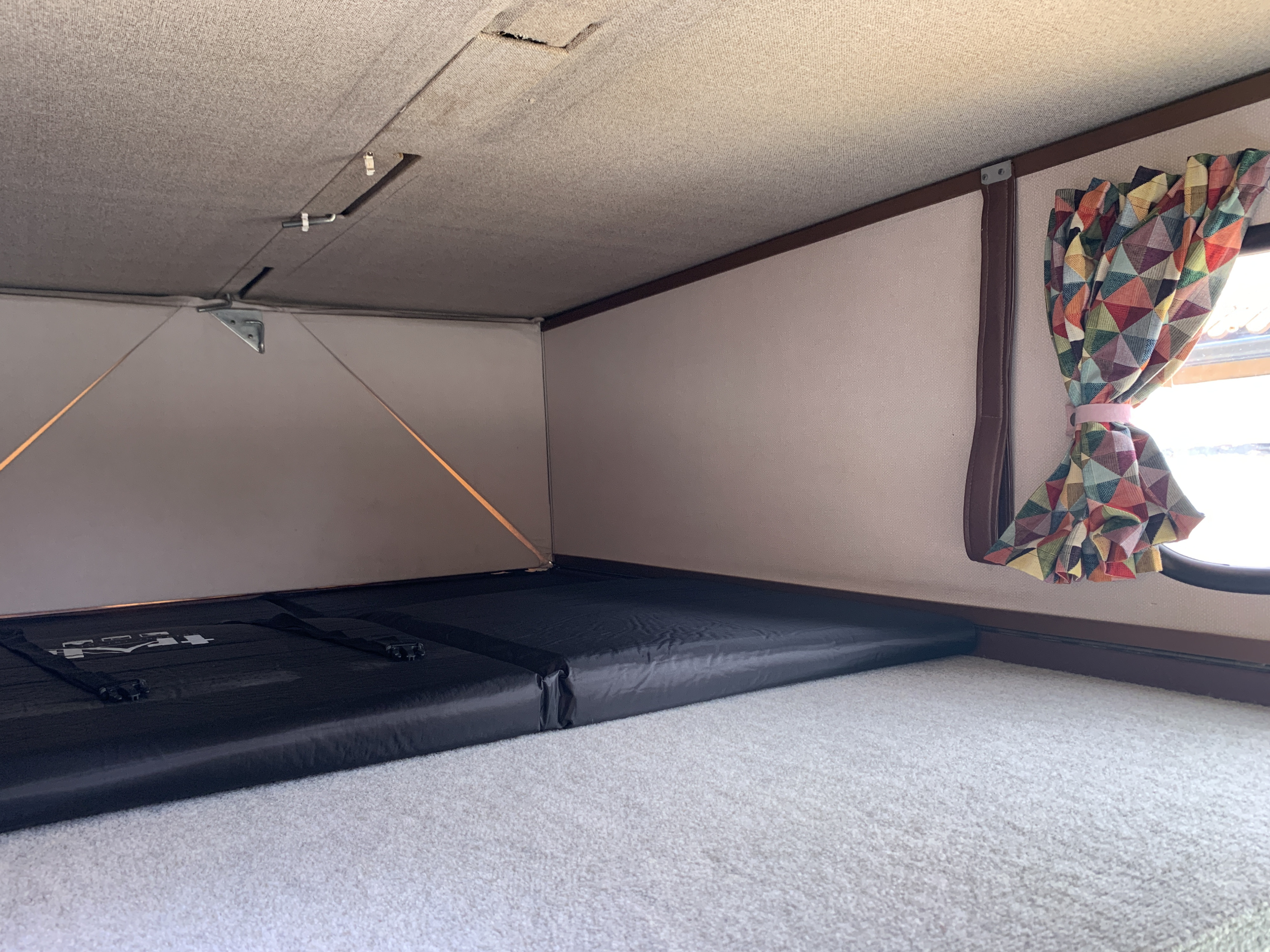 RV rental interior: A cozy sleeping area with a black mattress under a raised pop-top roof and colorful geometric window curtains.. Volkswagen Campervan 1989