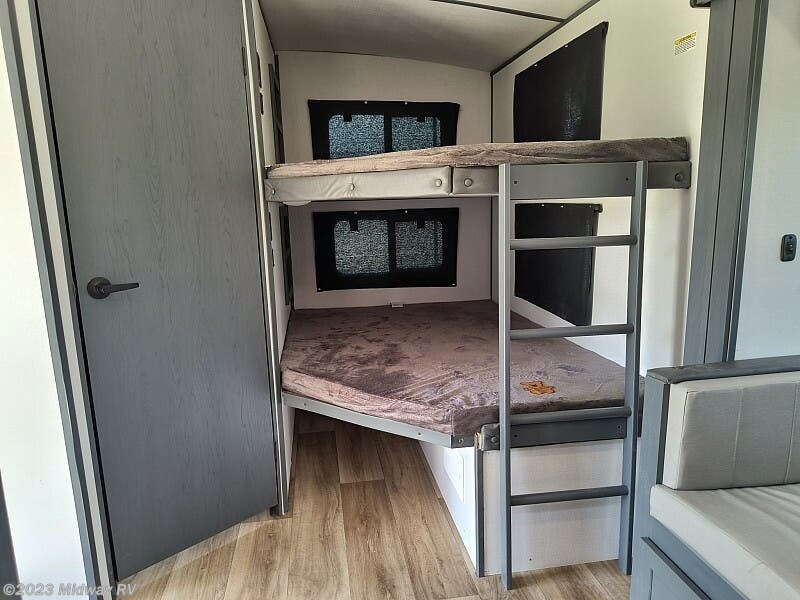 RV rental interior featuring a modern bunk bed setup with ladder, a door, and seating, ideal for comfortable sleep.. Keystone RV Bullet Ultra Lite 2023