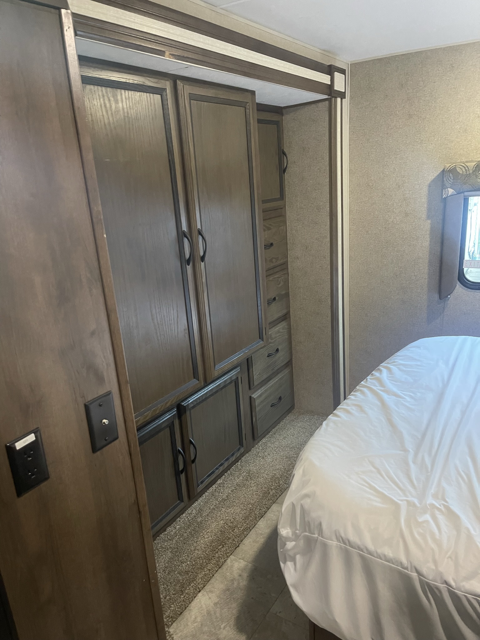 Inside an RV rental, this bedroom features a large wooden wardrobe and a white bed, ideal for comfort and storage.. Ford Coachman 2018