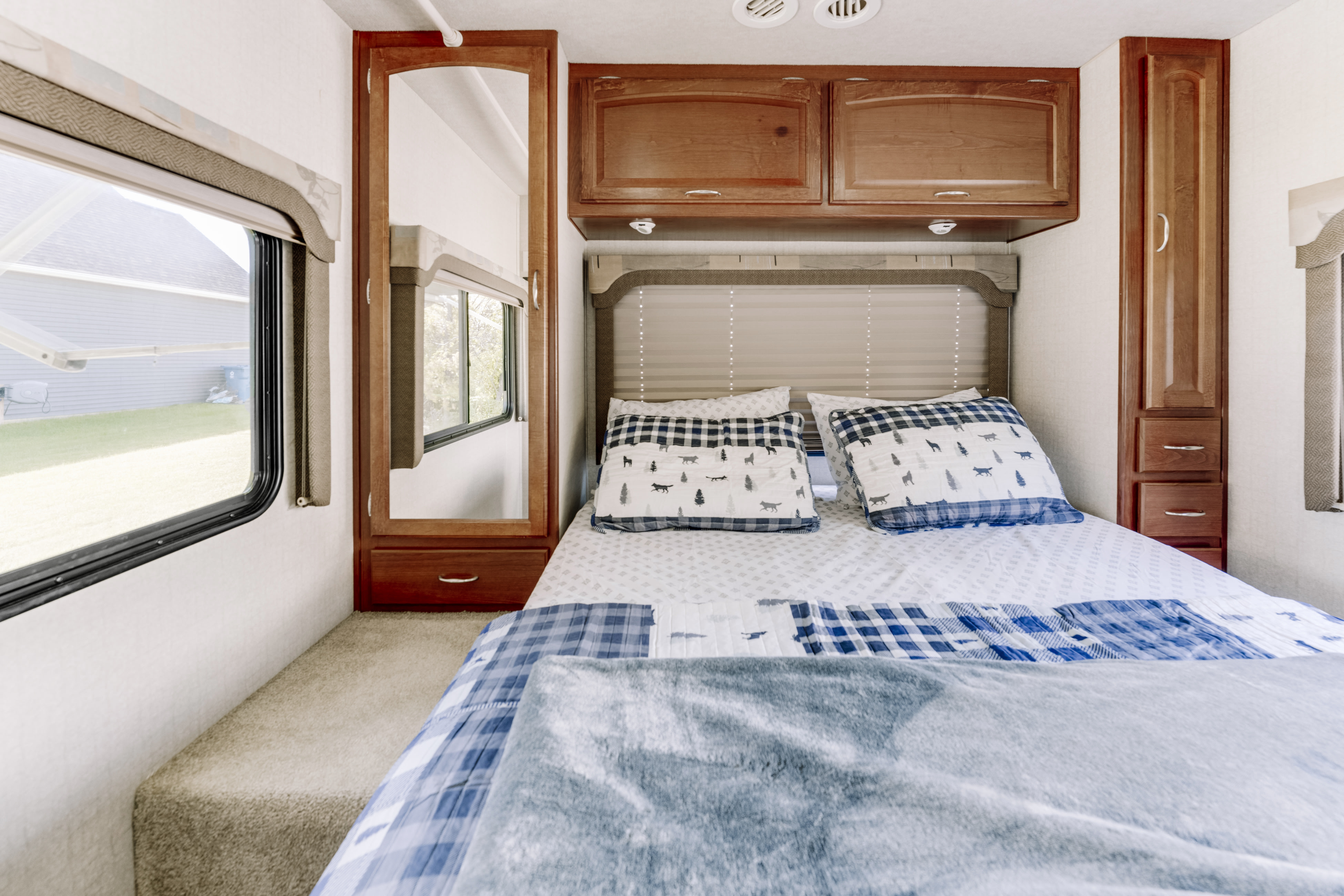 Cozy RV rental bedroom with blue plaid bedding, wooden cabinetry, and a window view.. Tioga Tioga Motorhome 2008