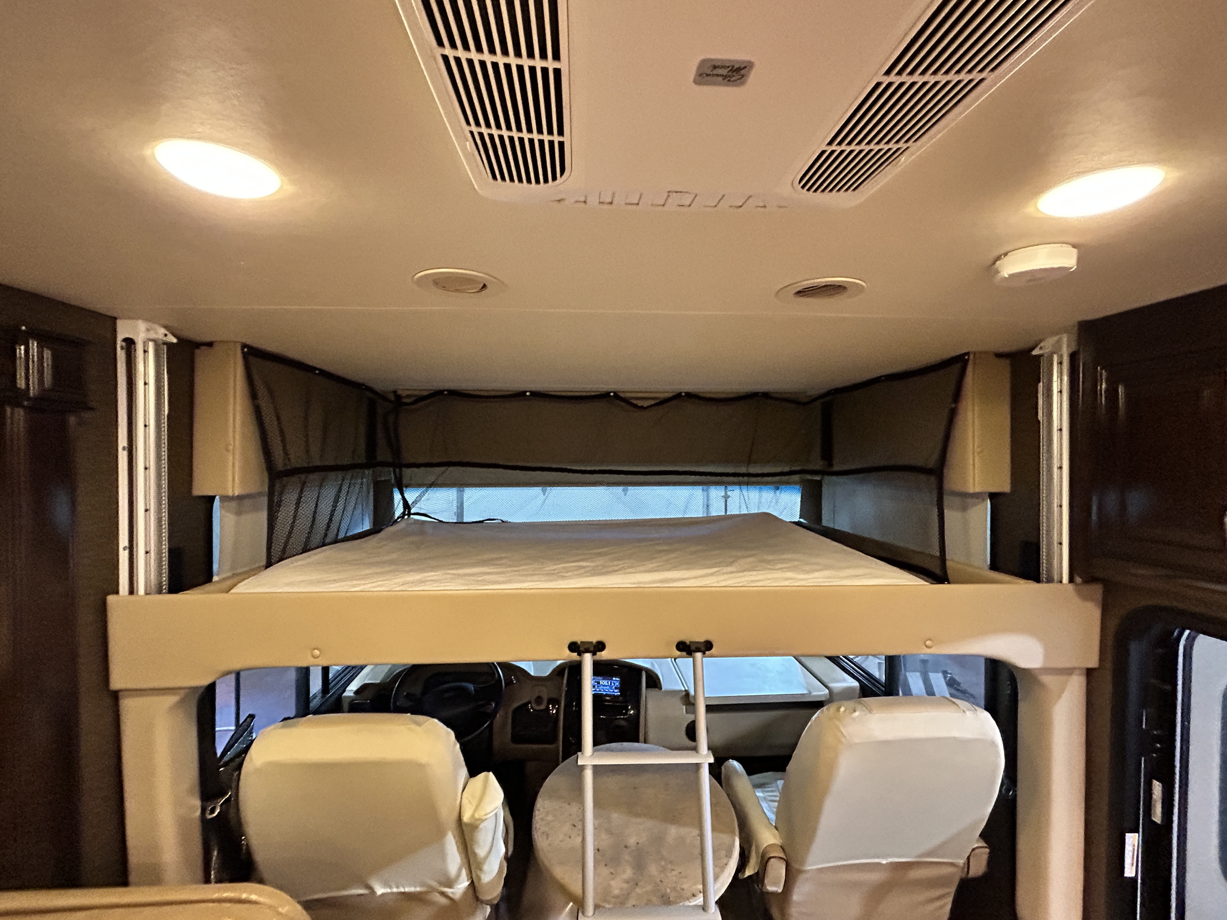 This RV rental interior shows a drop-down bunk bed above the front cockpit area with driver's seats and controls.. Thor Motor Coach Challenger 2016